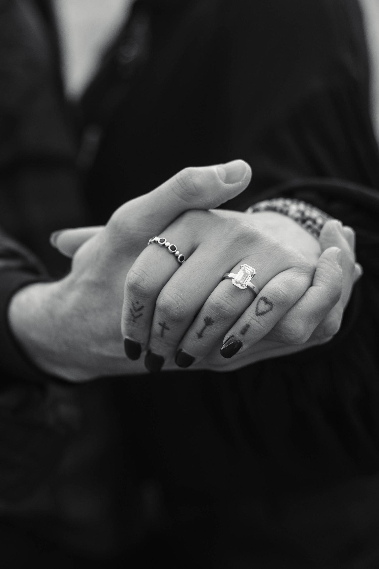 Close-up black and white photo of engaged couple holding hands showing emerald cut engagement ring in West Chester, PA.