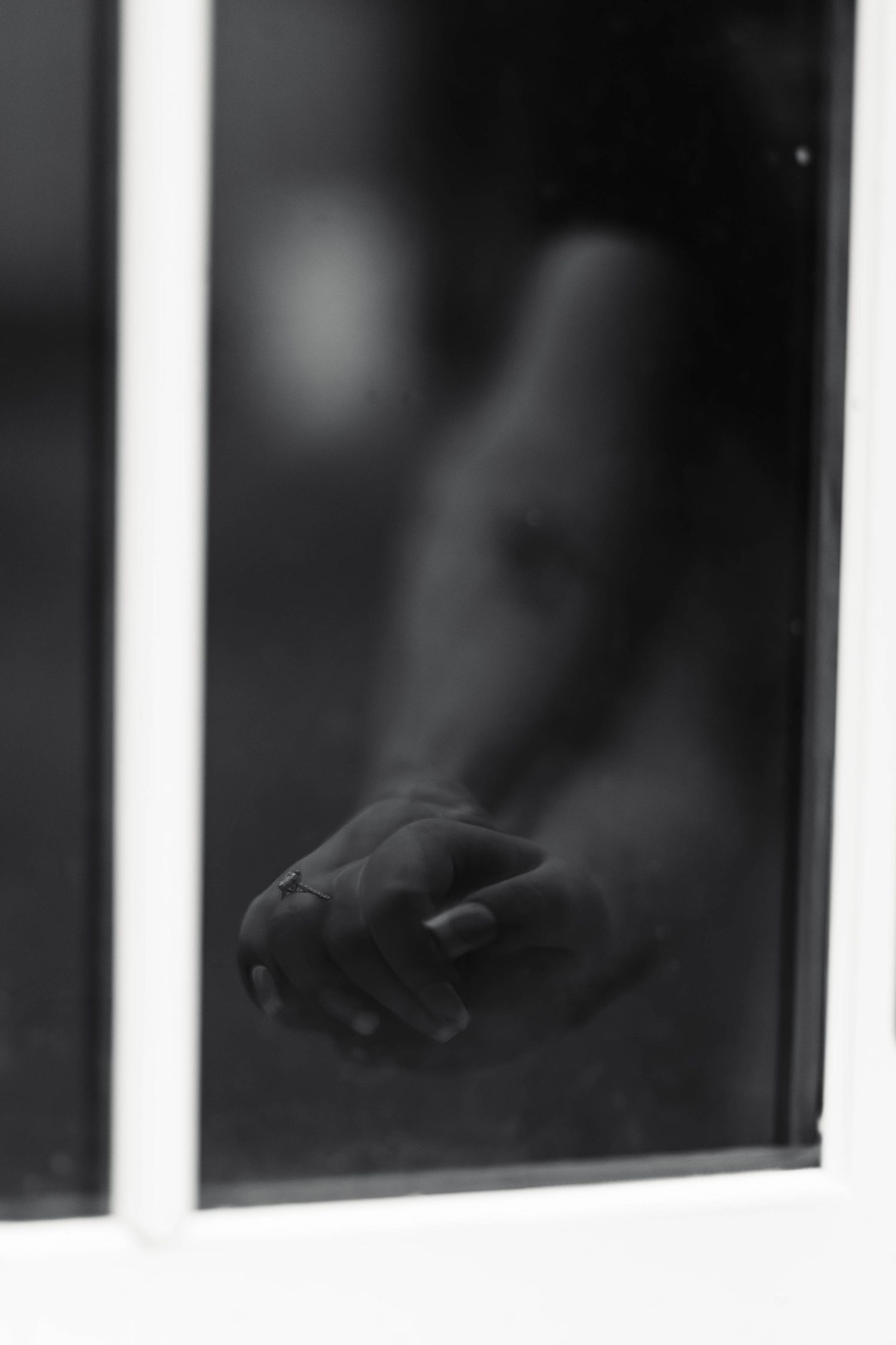 A black and white artistic silhouette of a hand with a ring pressed against a frosted glass window during an engagement session in Oley, PA.
