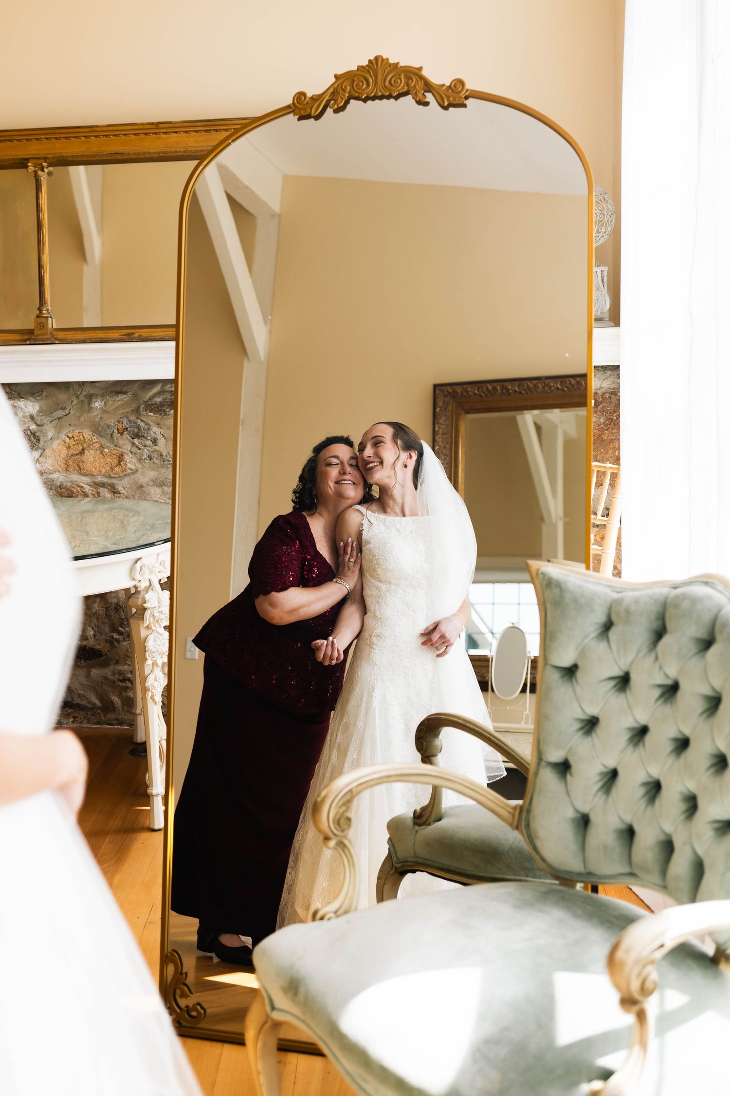 Mother and bride sharing a tender moment reflected in a large gold-framed mirror before ceremony.