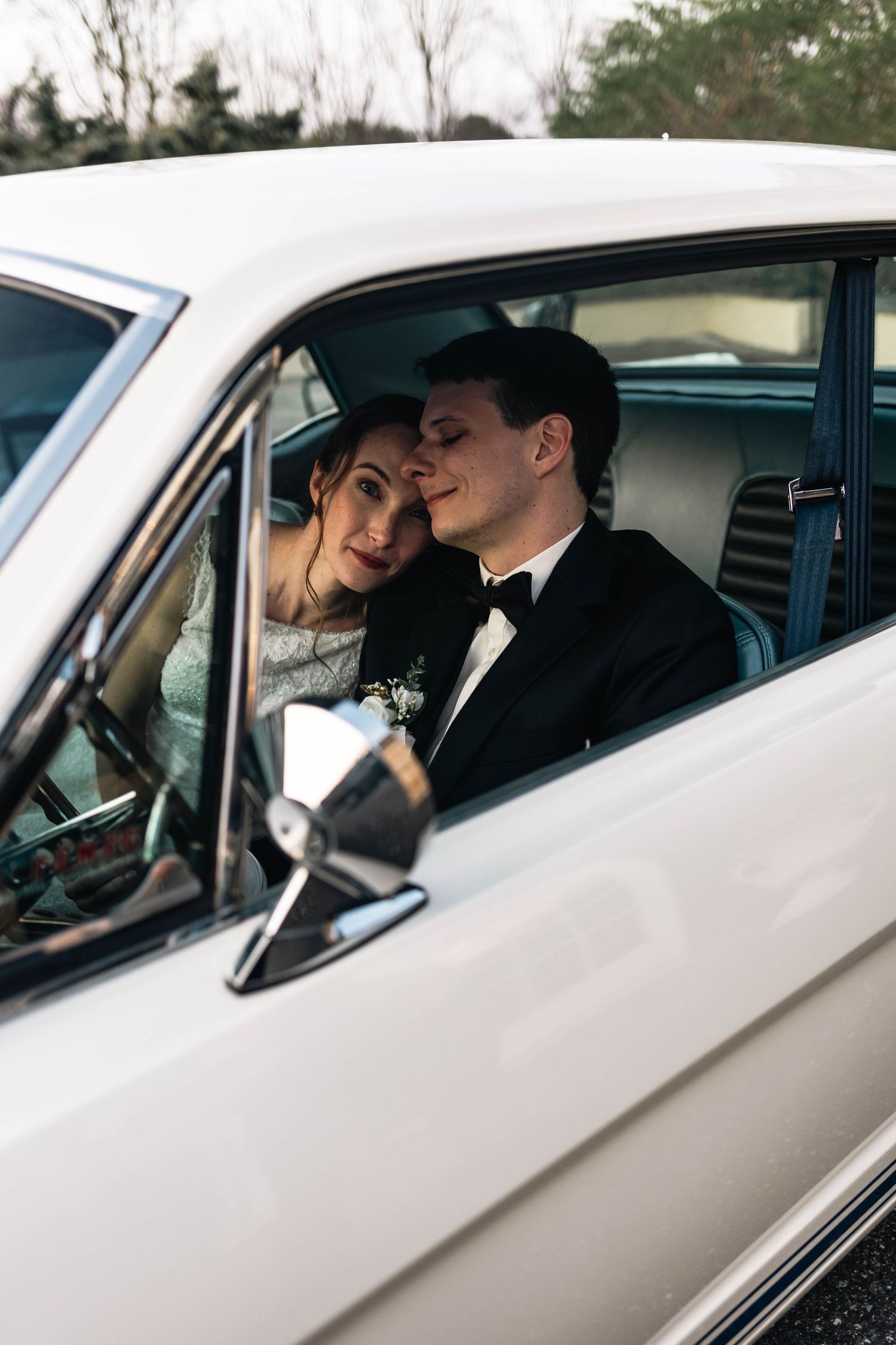Newlywed couple in wedding attire sharing a romantic moment inside a classic white vintage car in Philadelphia, PA.