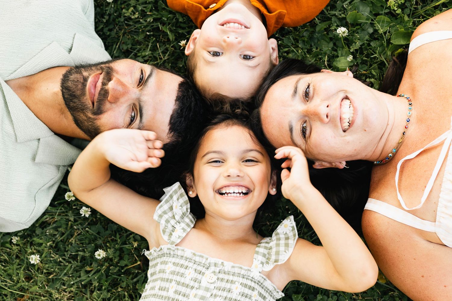 Family of four lying on grass in a circle smiling and laughing together outdoors at Reading Museum Arboretum.