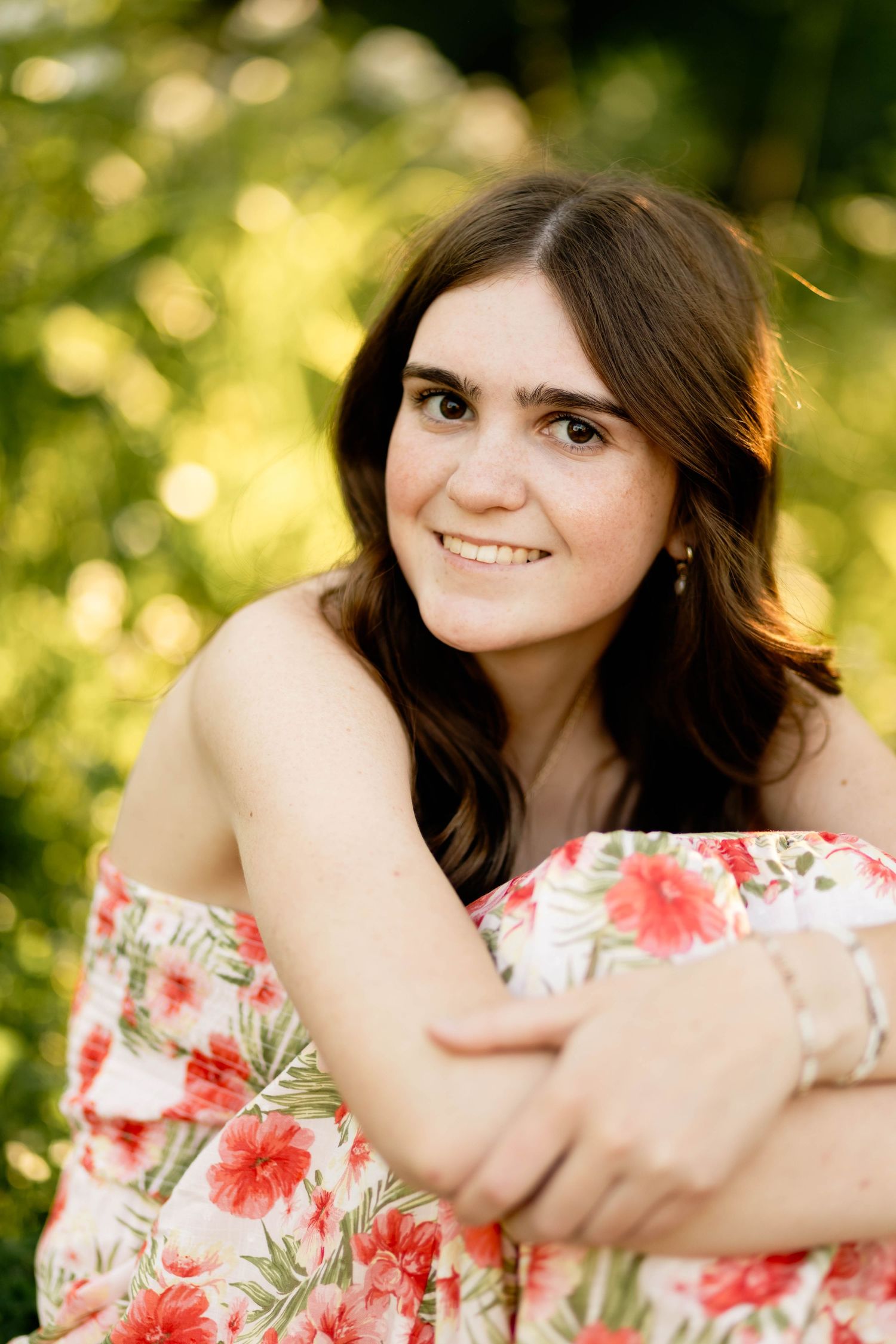 Smiling Boyertown Graduate in floral off-shoulder dress sitting outdoors in warm golden natural light.