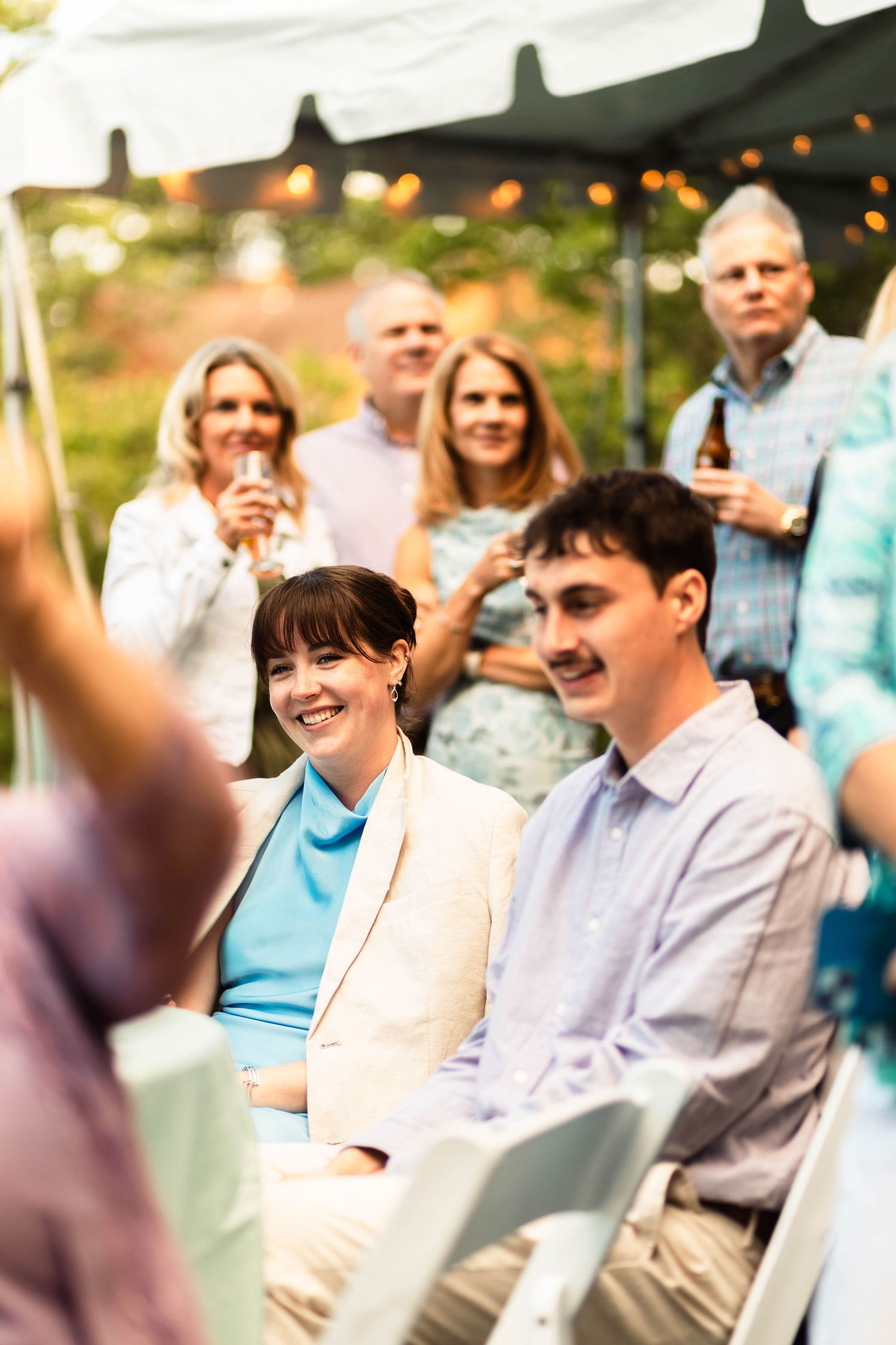 Wedding guests laughing and celebrating under a white tent with string lights at an outdoor reception.