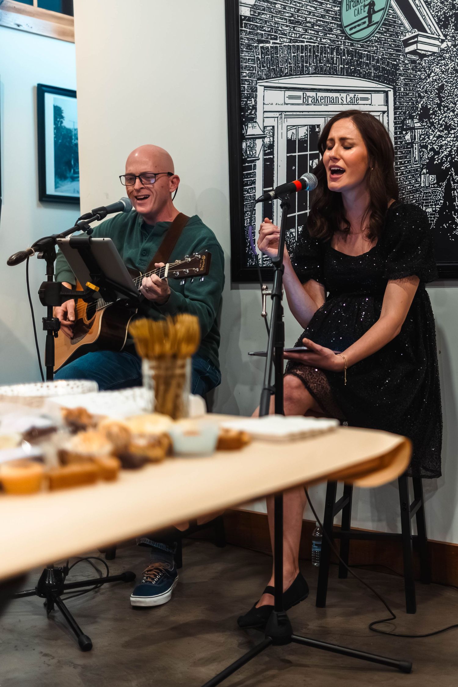 A man playing acoustic guitar and a woman singing into a microphone perform live music at Brakeman's Cafe in Boyertown, PA.
