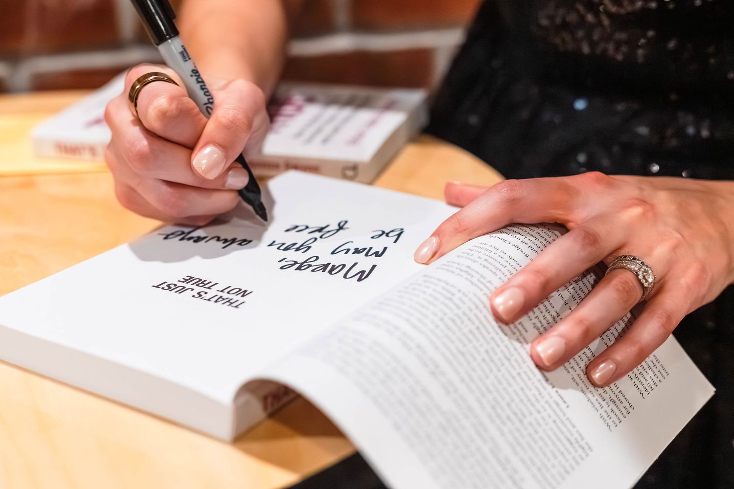 Author signing a book with a black pen at a book signing event.