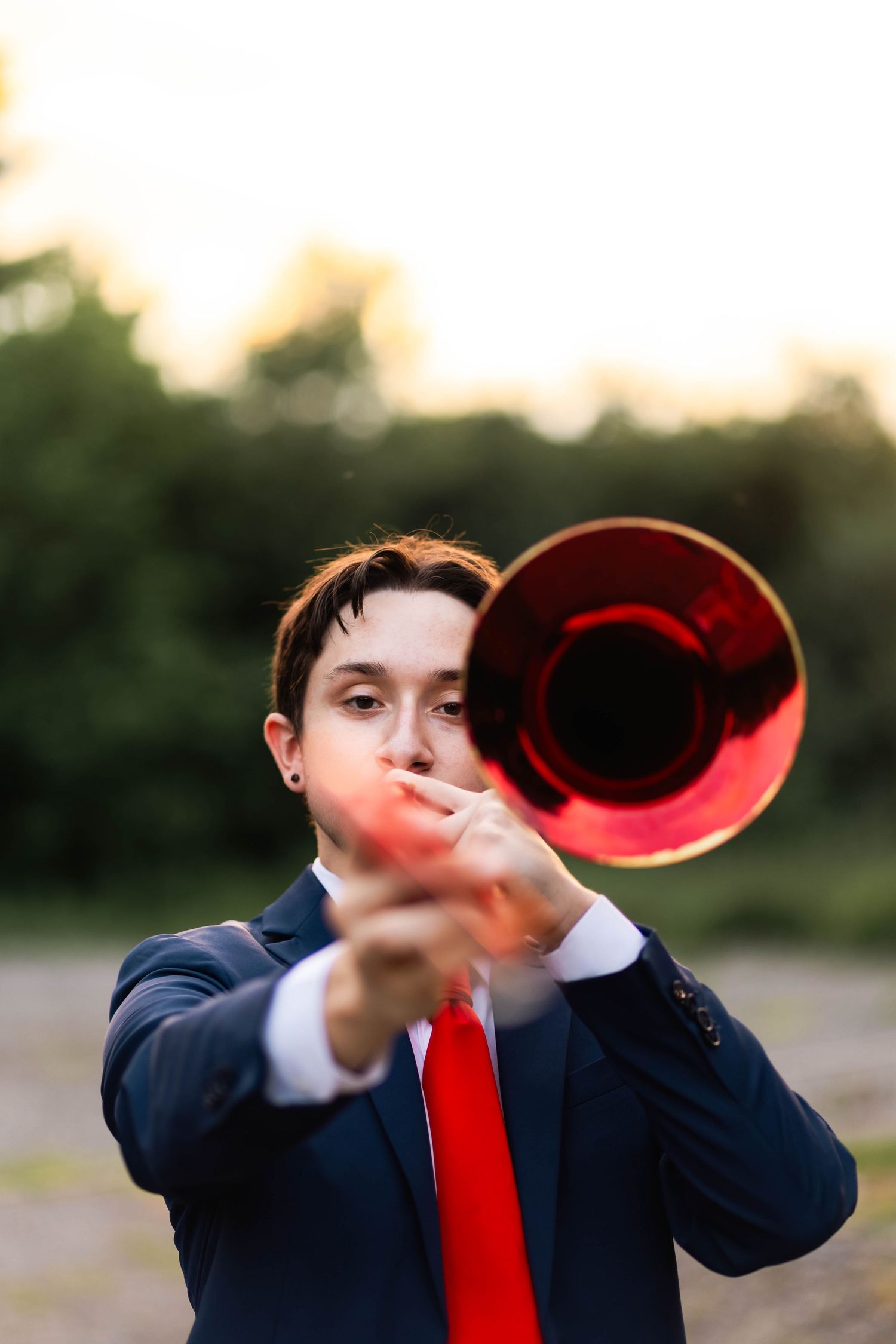 Owen J Roberts High School Senior in navy suit plays red trombone directed toward camera outdoors.