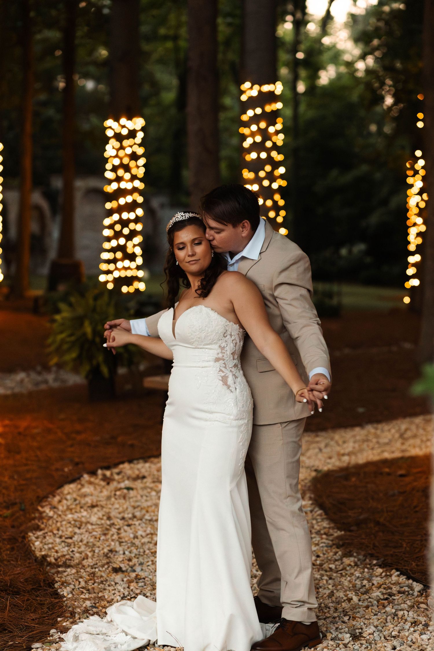 Bride and groom share a tender dance surrounded by glowing string lights wrapped around tall pine trees.
