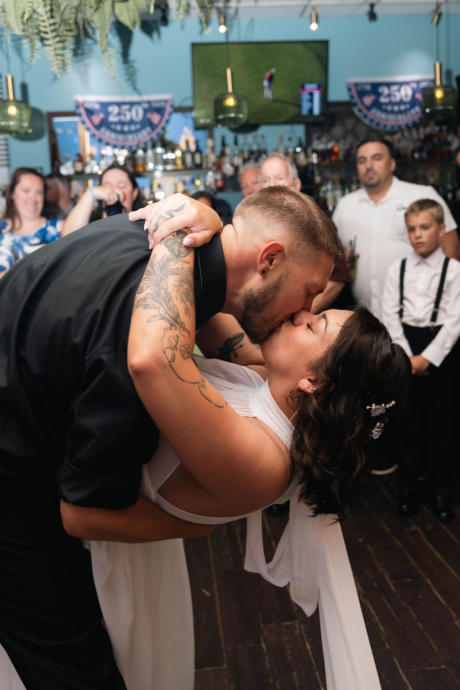 Groom dipping bride for a passionate kiss on the dance floor surrounded by wedding guests at reception.