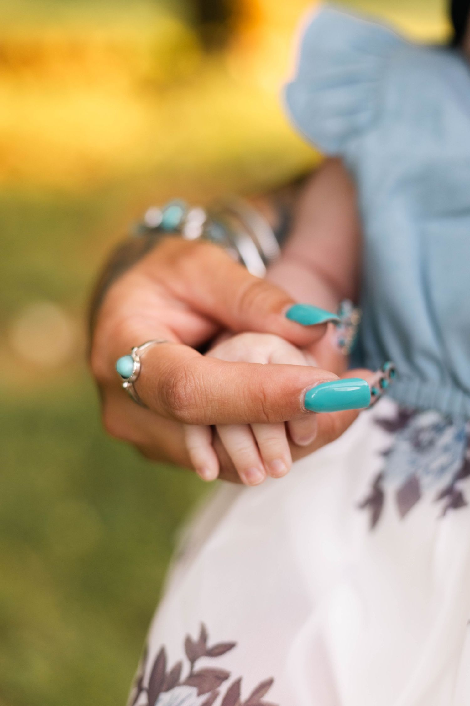 Close-up of mother's hand with turquoise nails and rings gently holding tiny newborn baby fingers during a newborn session in Boyertown, PA