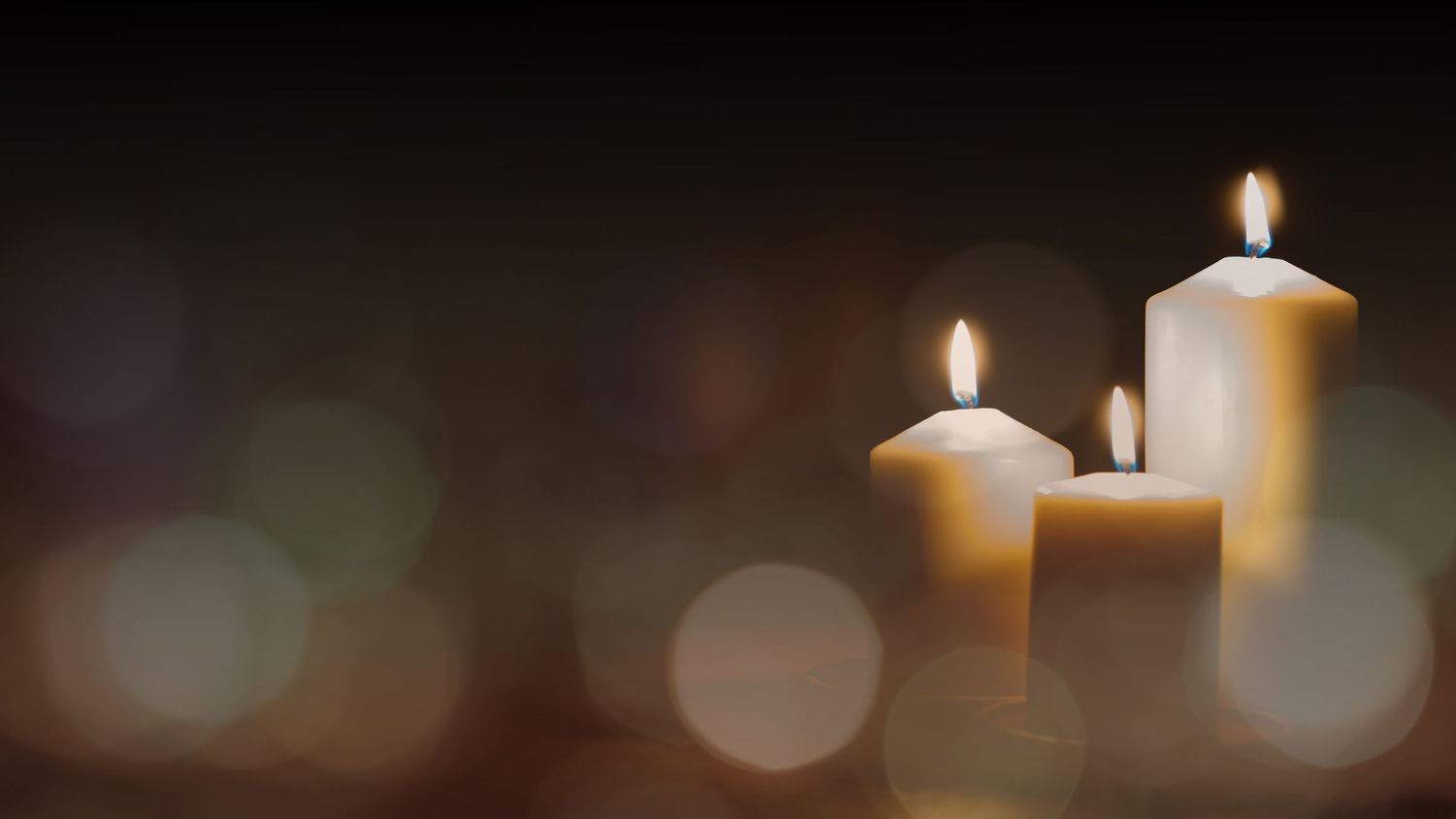 Three glowing white candles with soft bokeh lights creating a warm and tranquil atmosphere against dark background.