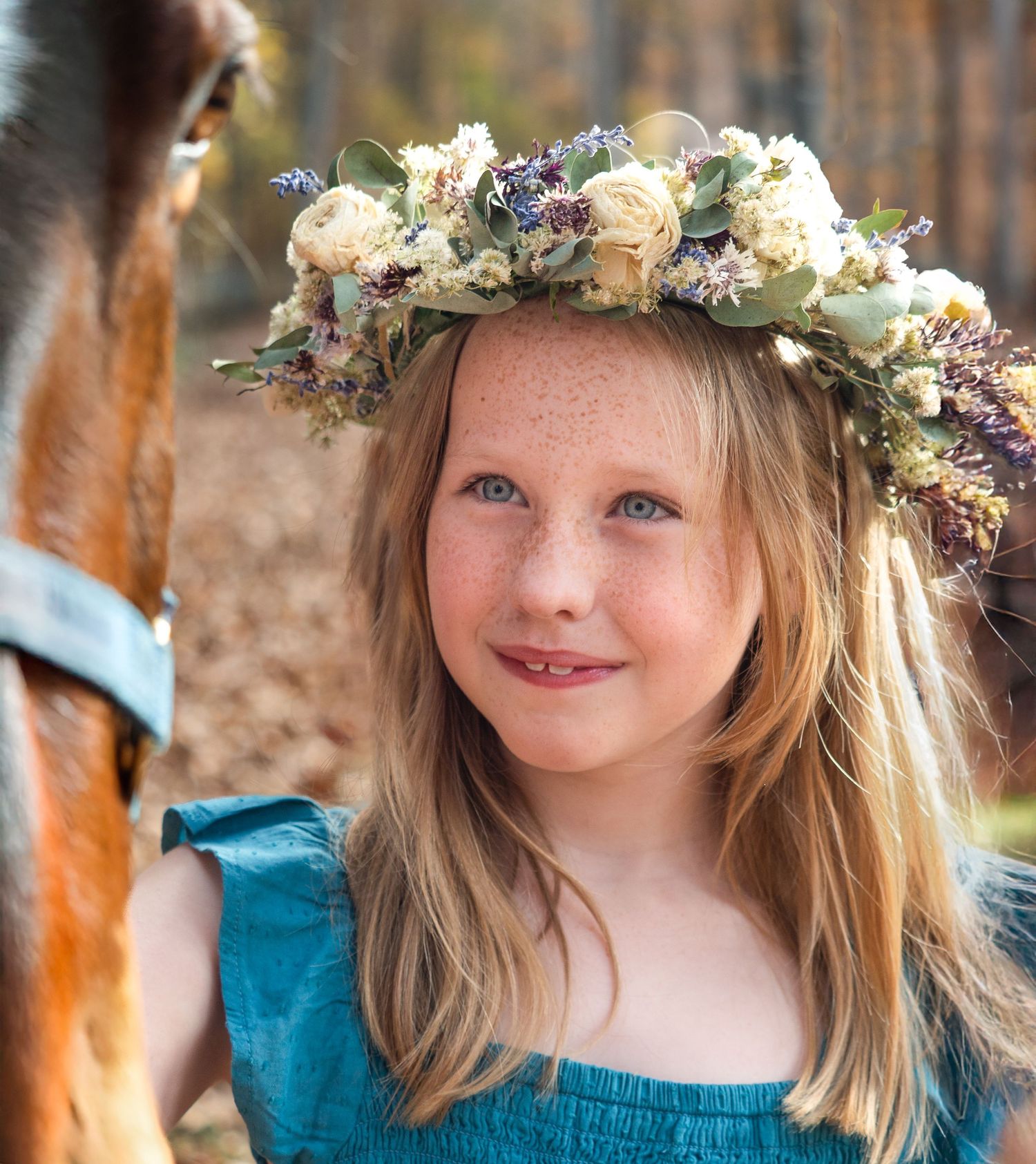 Photo of a youg girl wearing a flower crown as she lovingly looks at her horse.