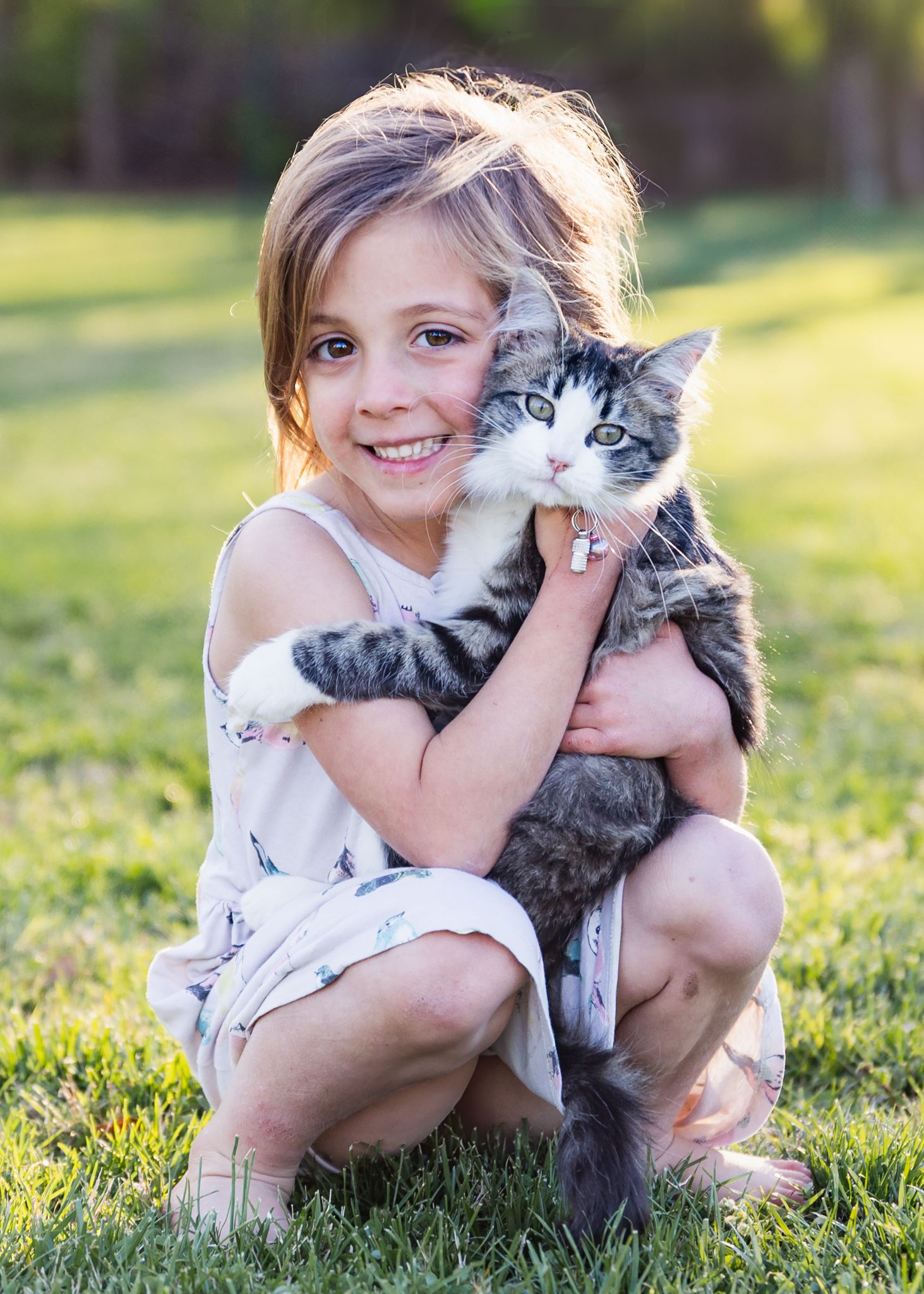Photo of a young girl hugging her cat shot on her farm. The girl is squatting on the ground in a natural pose.