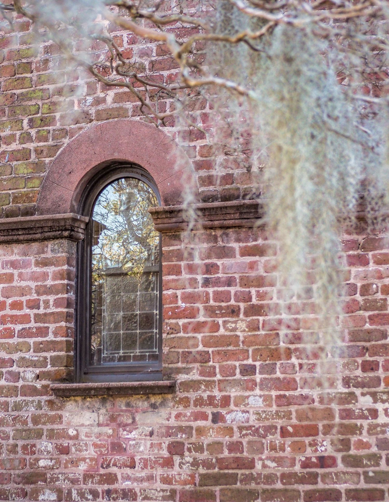 Photograph of a historic red church in Charleston South Carolina. The arched window is framed by Spanish moss.