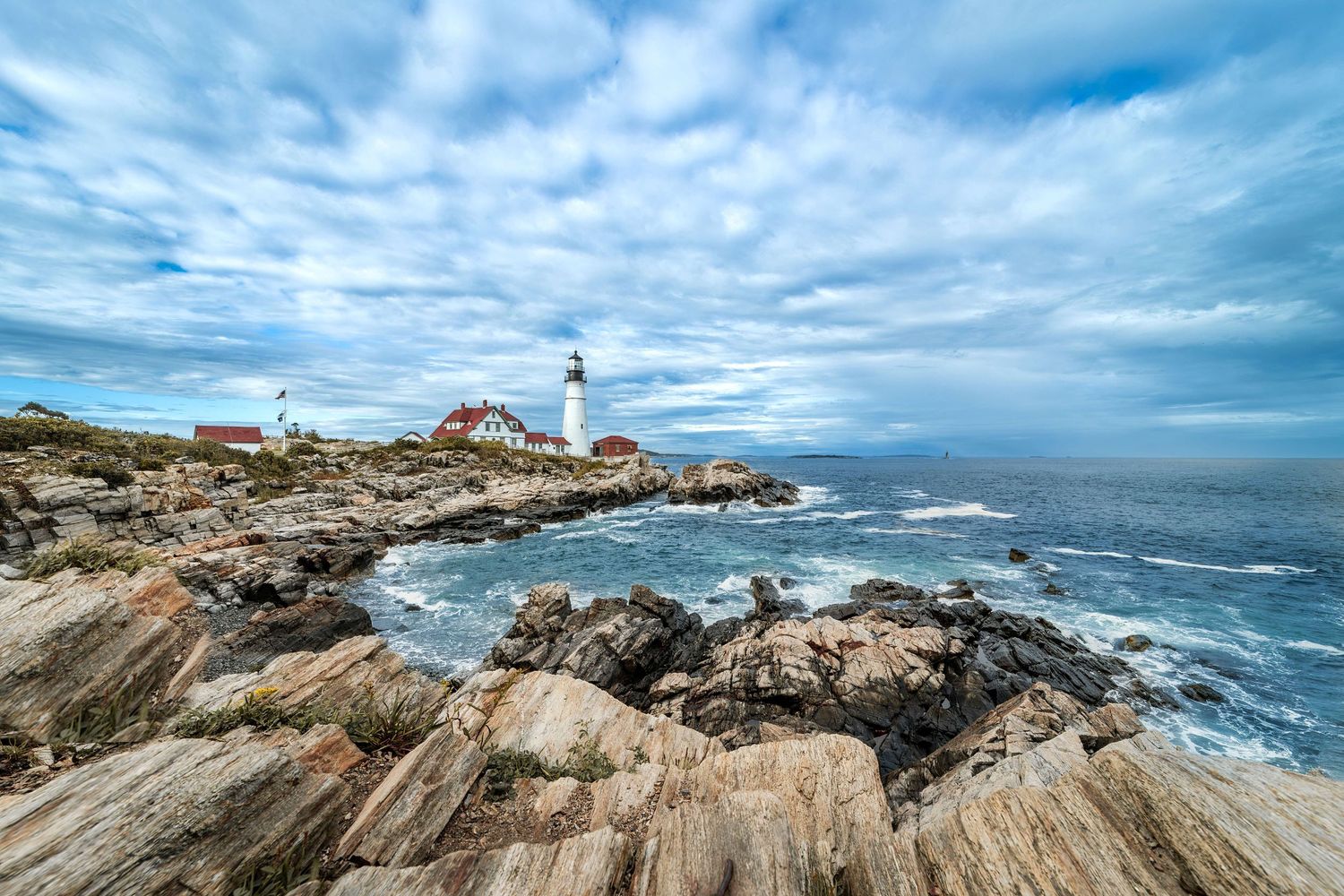 Photo of Portland Headlight Lighthouse Main. Wide angle view showing the rocks in the foreground and a dramatic sky behind the lighthouse.