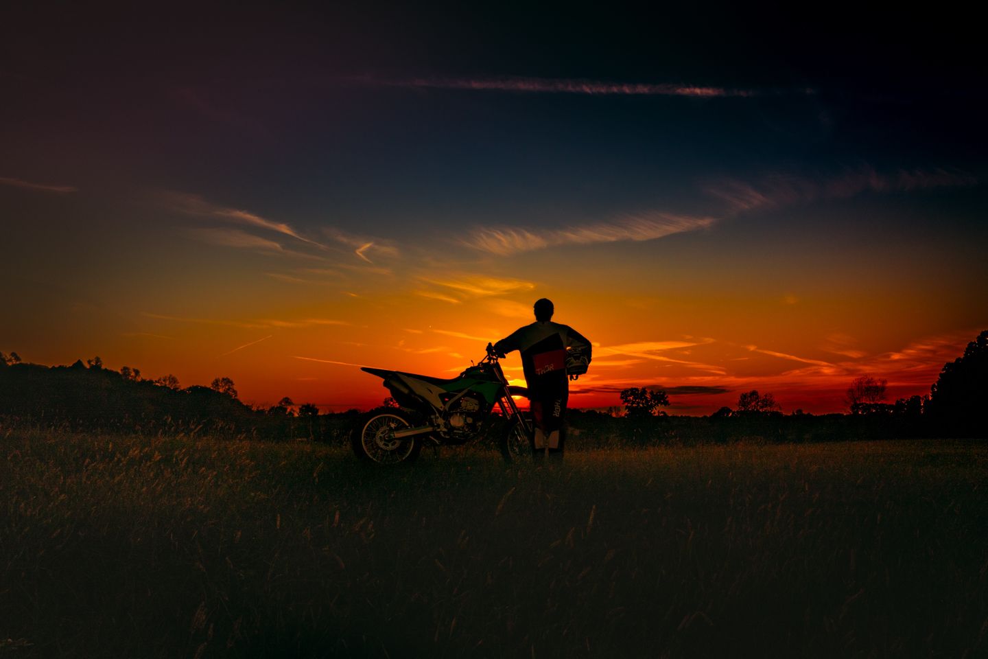 Photo of a young man with his motocross bike shot in silhouette at sunset on his family's farm in Tennessee