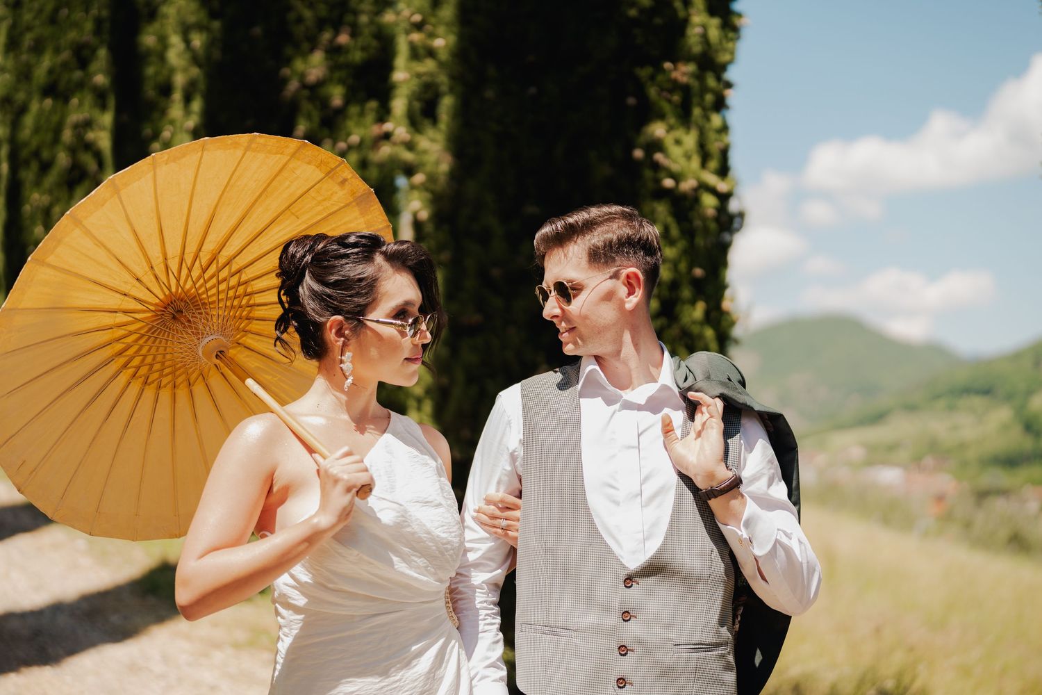Para młoda spaceruje po alei cyprysów w Toskanii, fotograf ślubny uchwycił romantyczną chwilę i naturalne emocje.