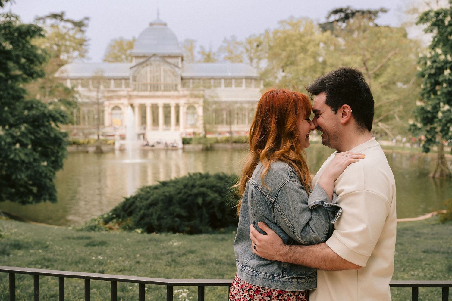 A couple shares romantic moments in front of a grand palace and lake with ornate classical architecture.