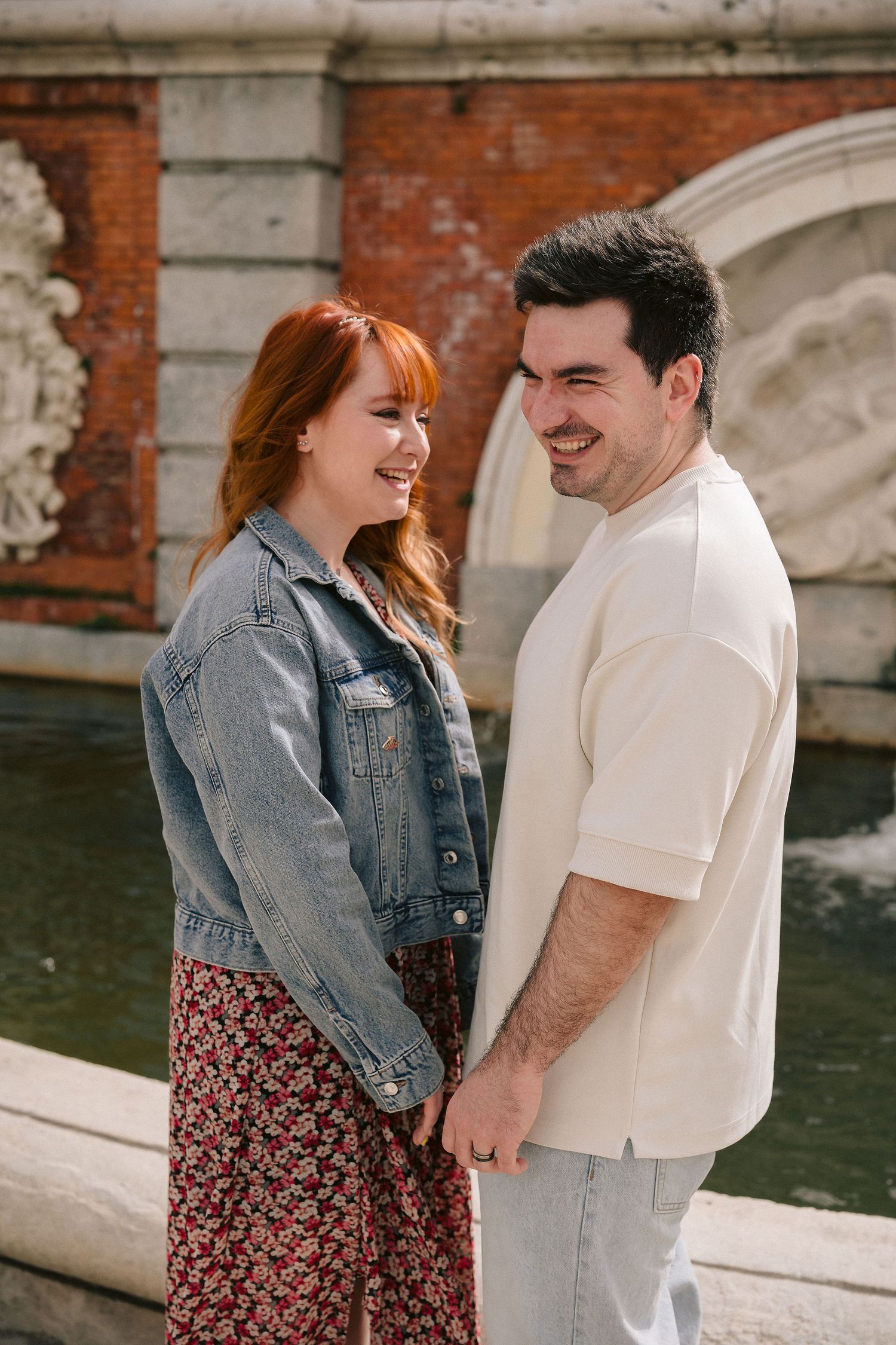 A couple shares laughter while posing against a brick wall background.