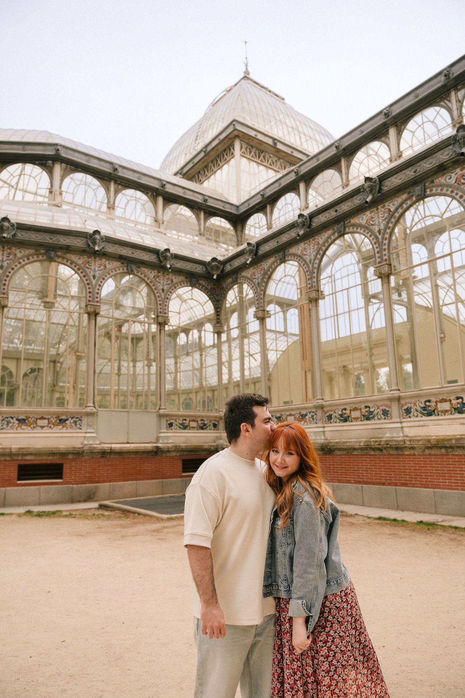 A pair stands before the ornate Crystal Palace glass structure in Retiro Park.