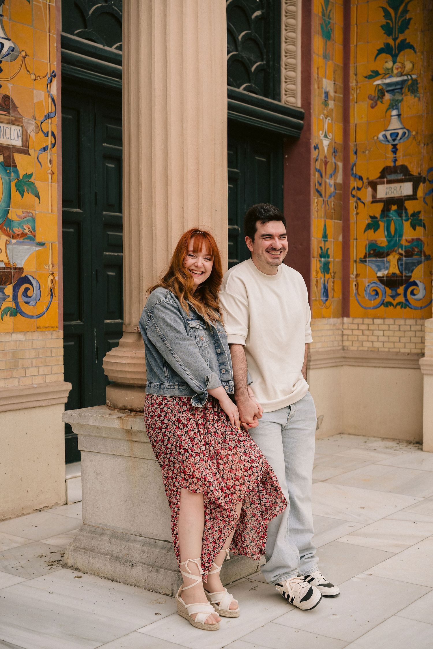 A couple sits together against a yellow wall with decorative painted details and columns.