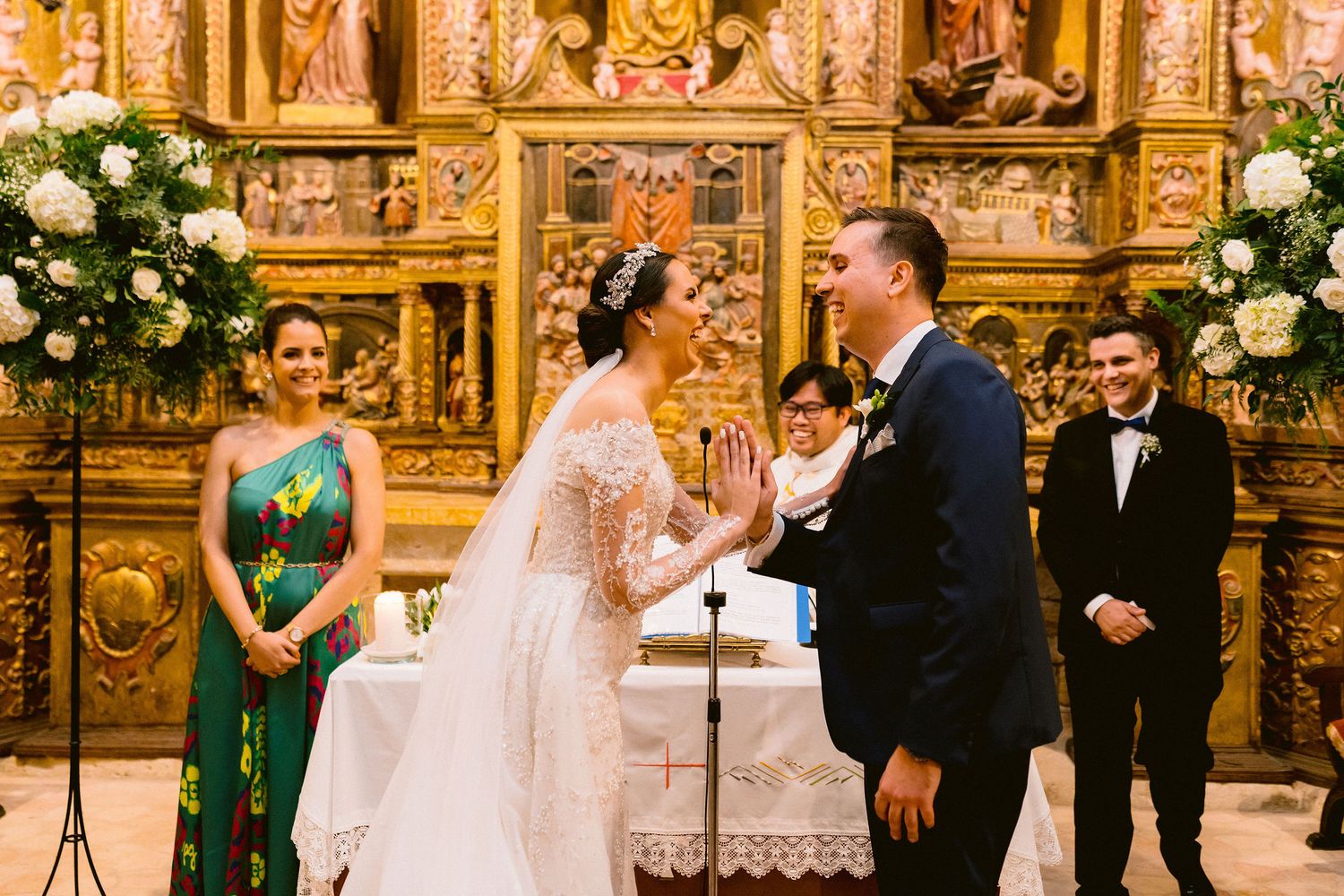 Traditional wedding ceremony taking place in an ornate golden church altar with floral arrangements and formal attire.