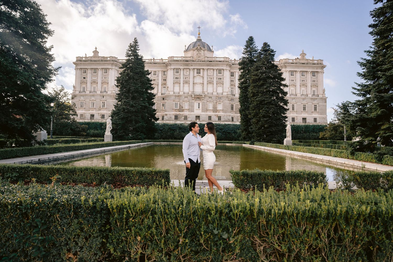 A romantic photoshoot at a grand palace with manicured gardens and reflecting pool.