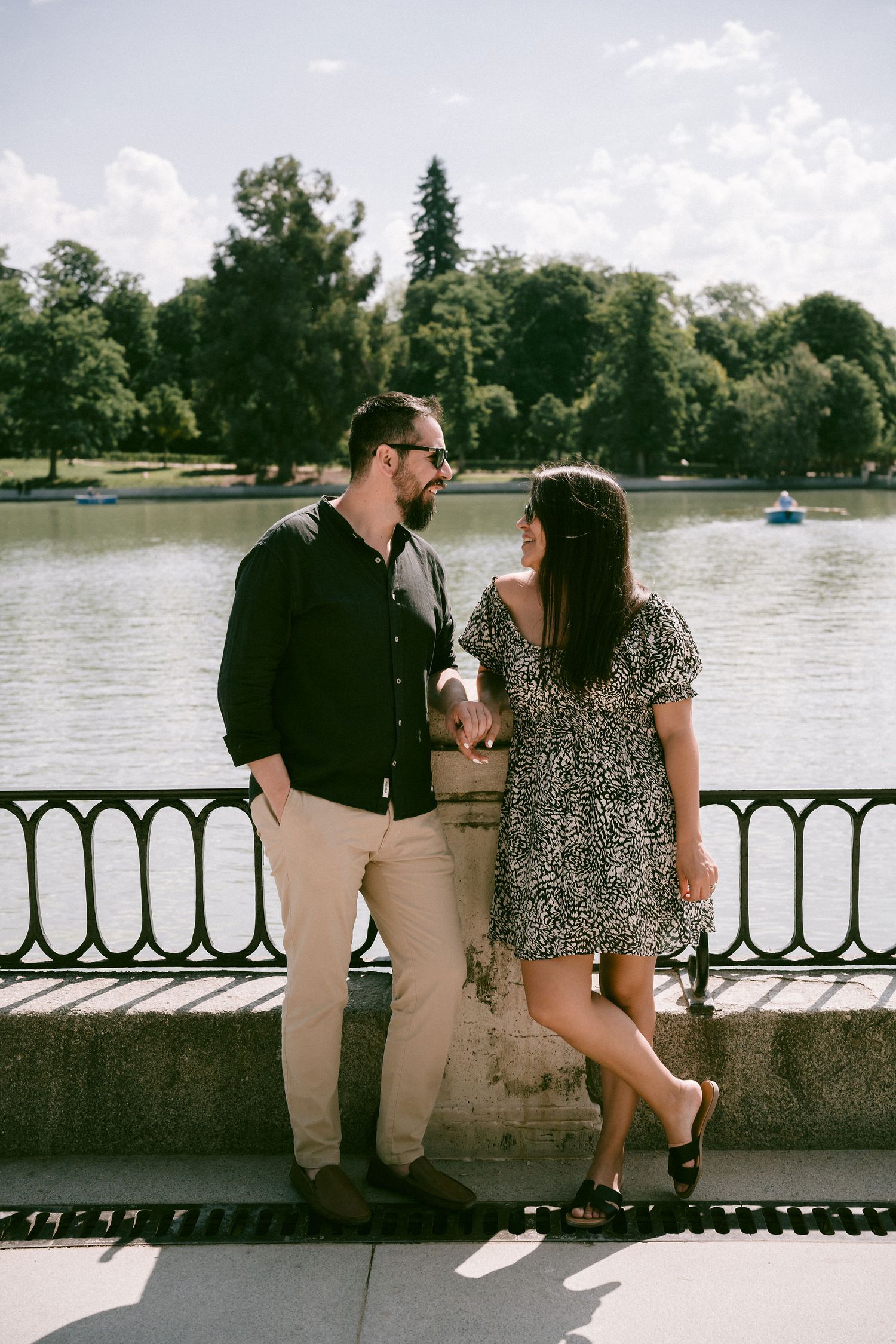 A couple shares an intimate moment while standing by a lake with ornate railing.