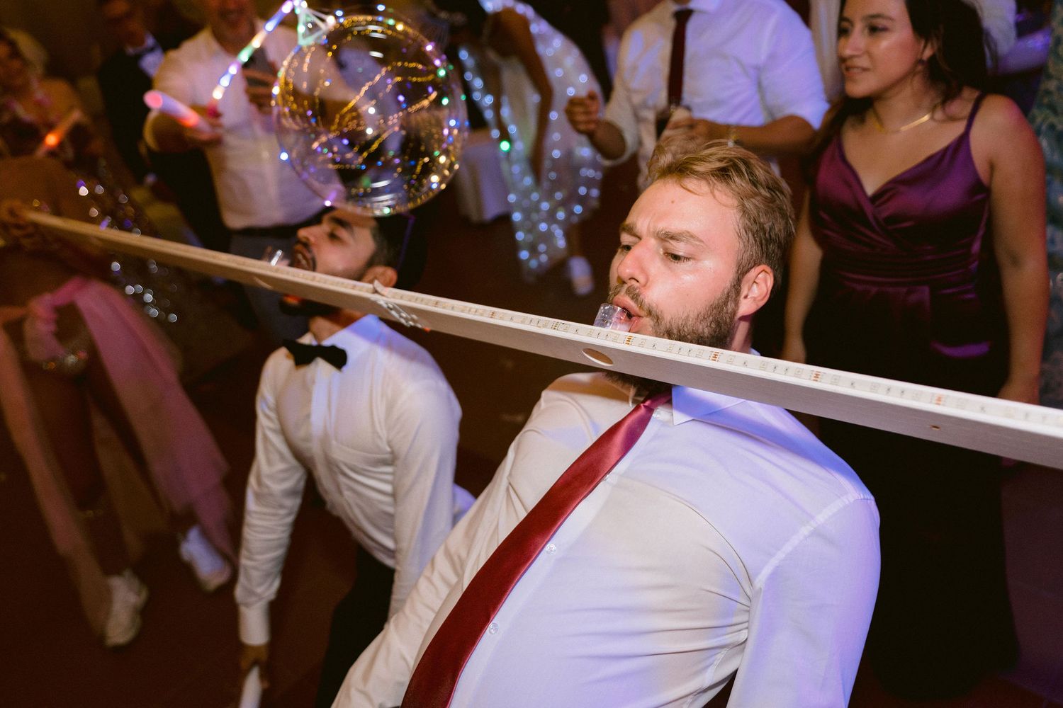 A group of wedding guests dance on a dance floor while holding ribbons during a celebration.
