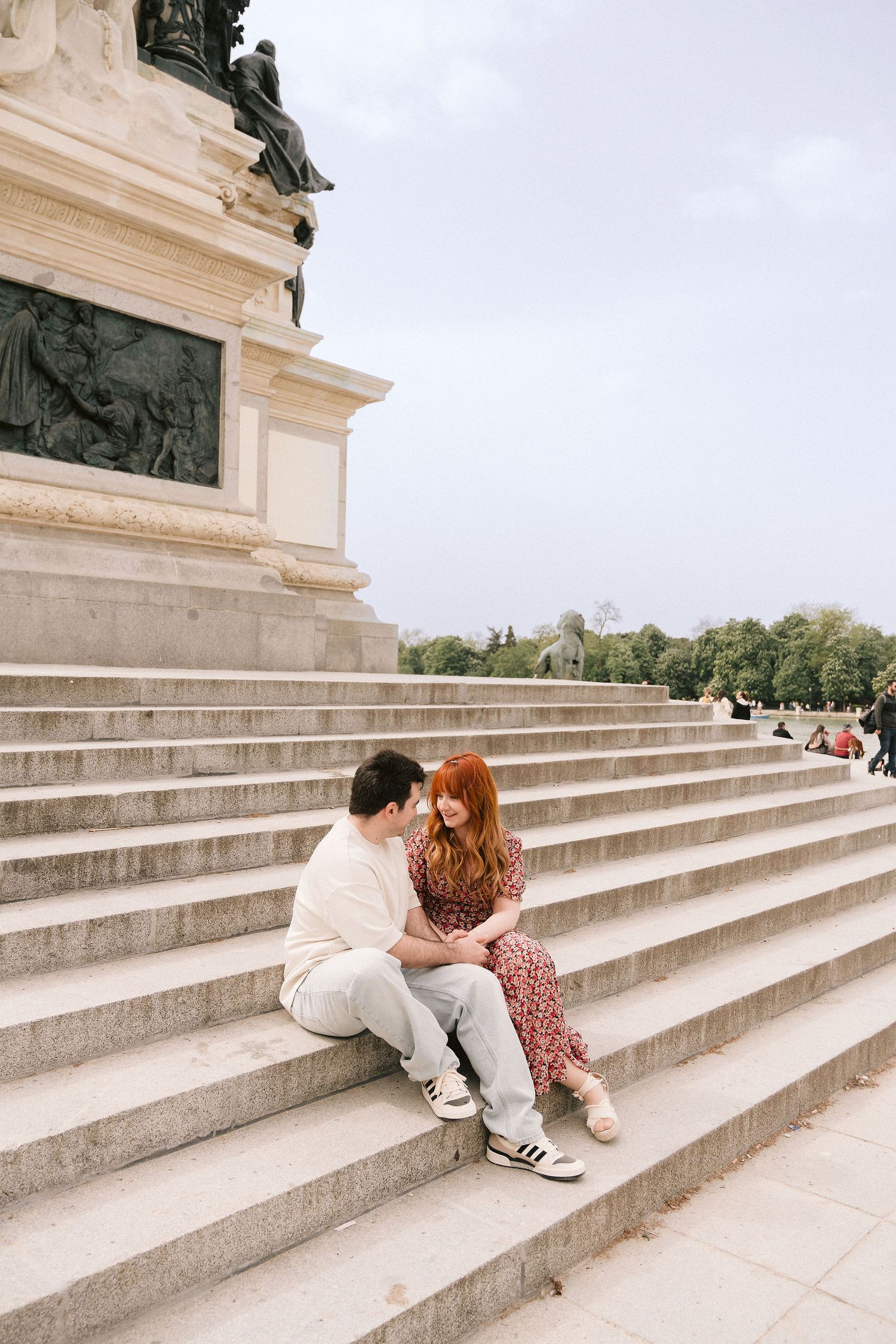 A couple sits together on grand stone steps in a European park setting.