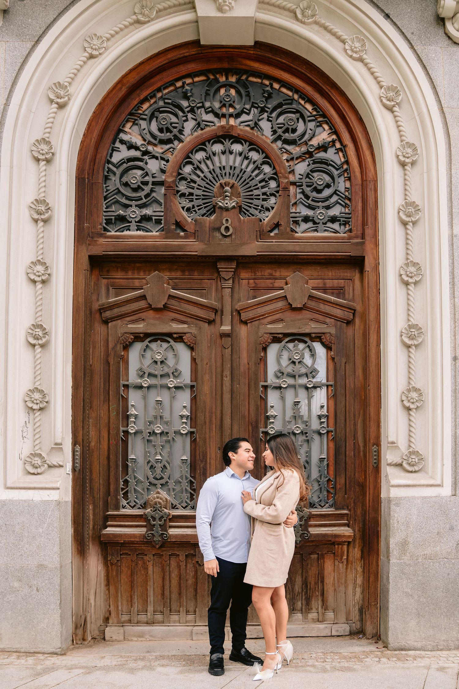A couple poses in front of an elaborately carved wooden door with ornate metalwork.