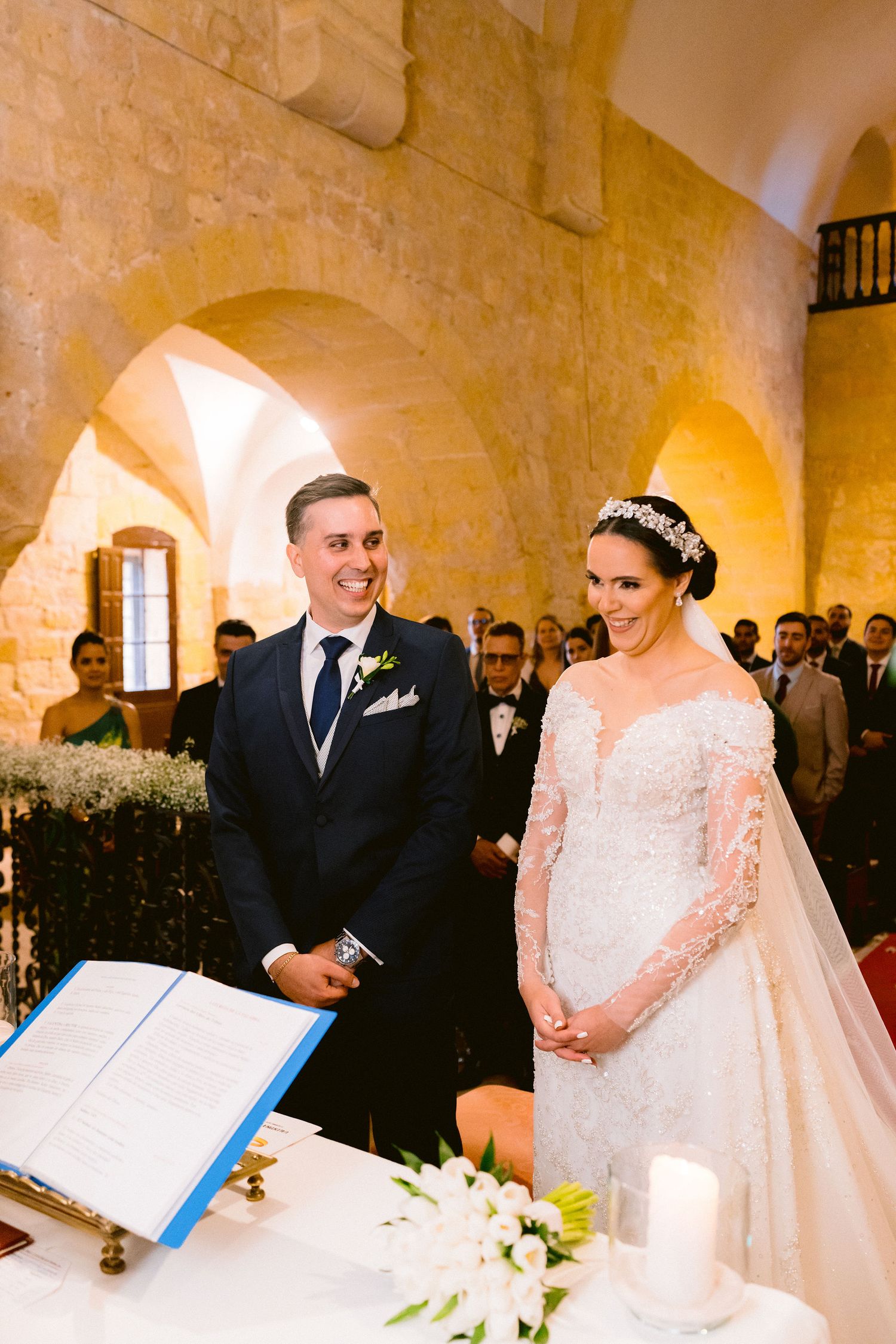A traditional wedding ceremony takes place inside a historic stone building with arched architecture and warm lighting.