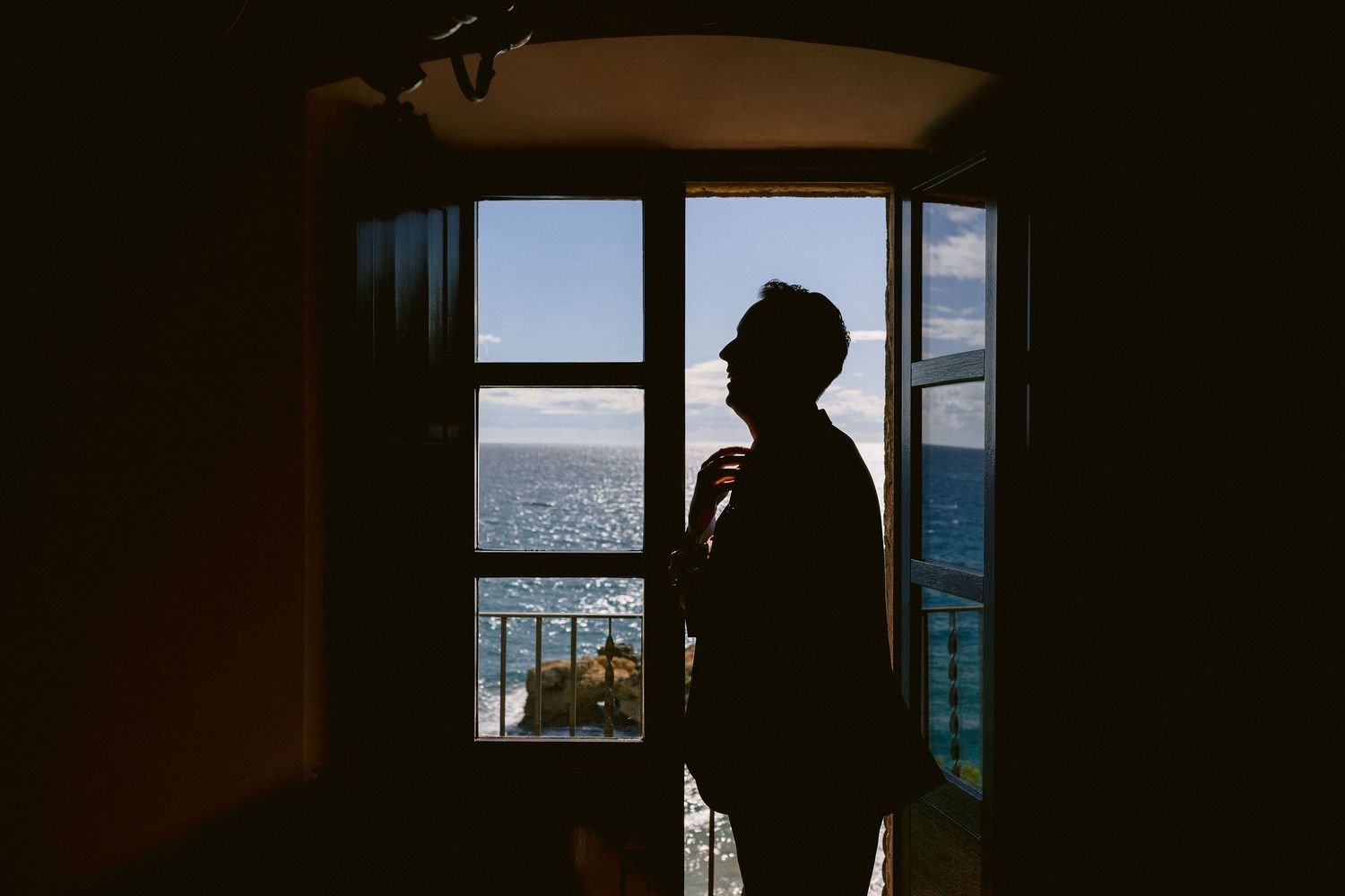 Dark silhouette against an open window looking out at blue ocean views during daylight.