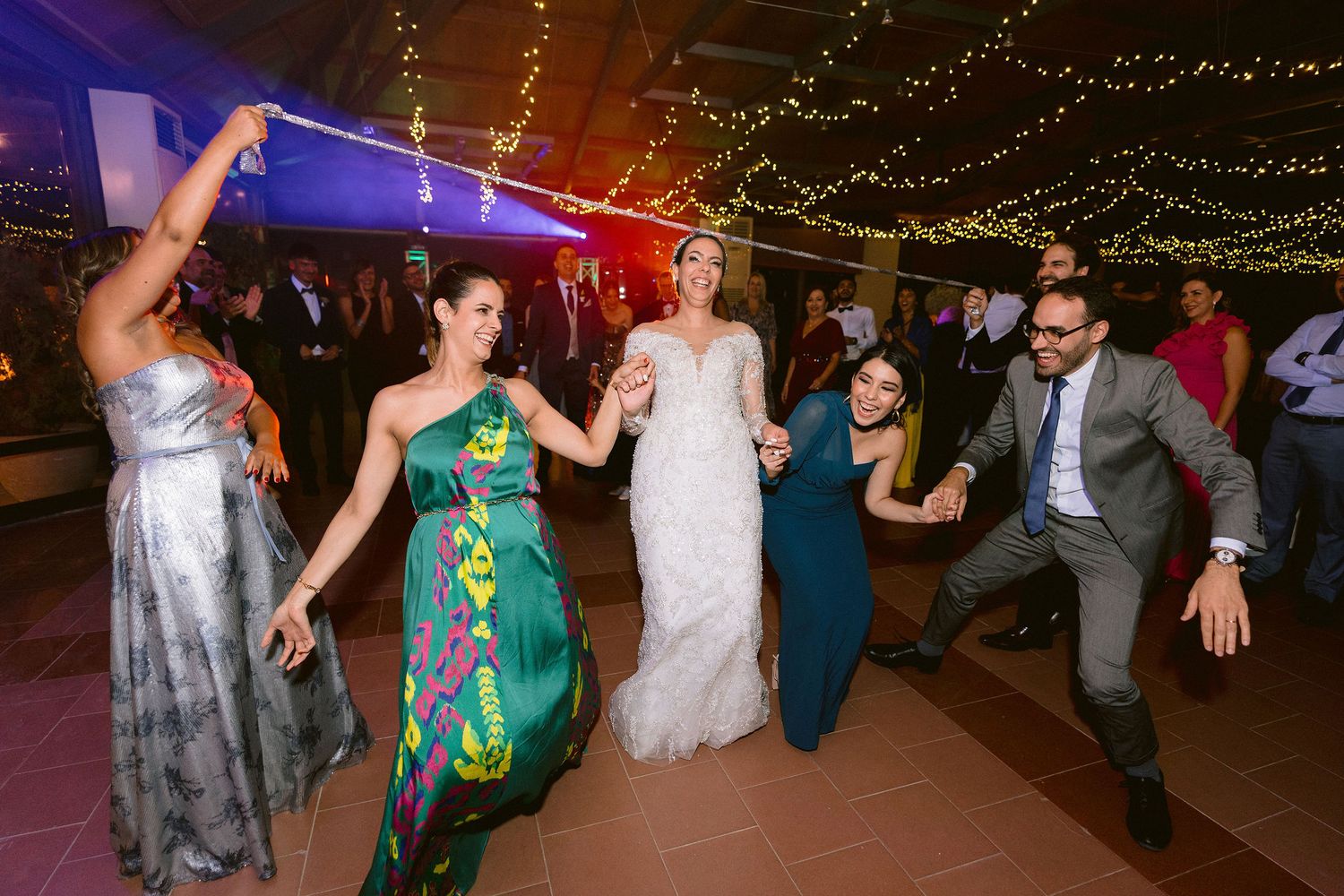 Wedding reception guests dance together under string lights at an outdoor evening celebration.