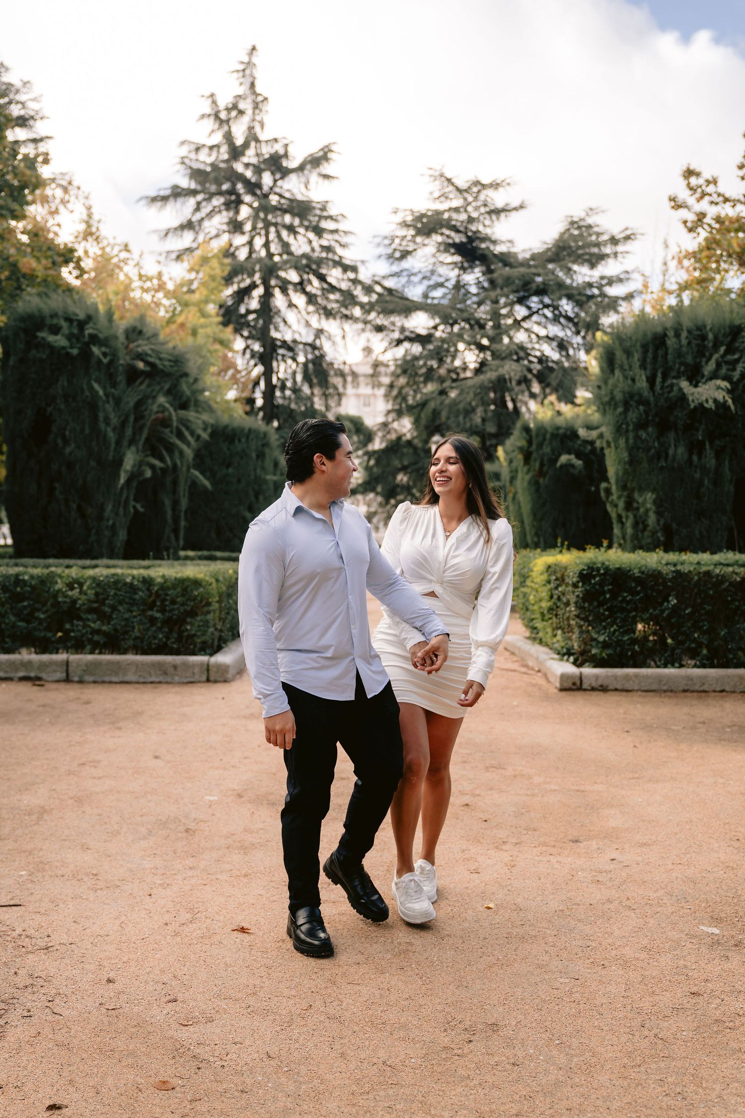 A couple walks hand in hand through a manicured garden path.