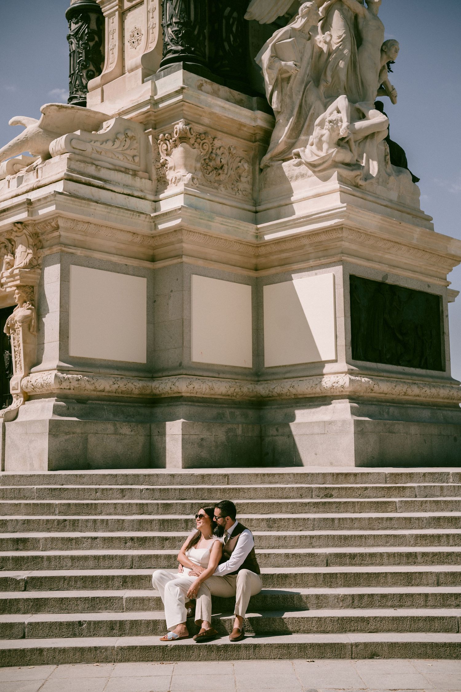 A couple sits intimately on grand stone steps of a classical monument.
