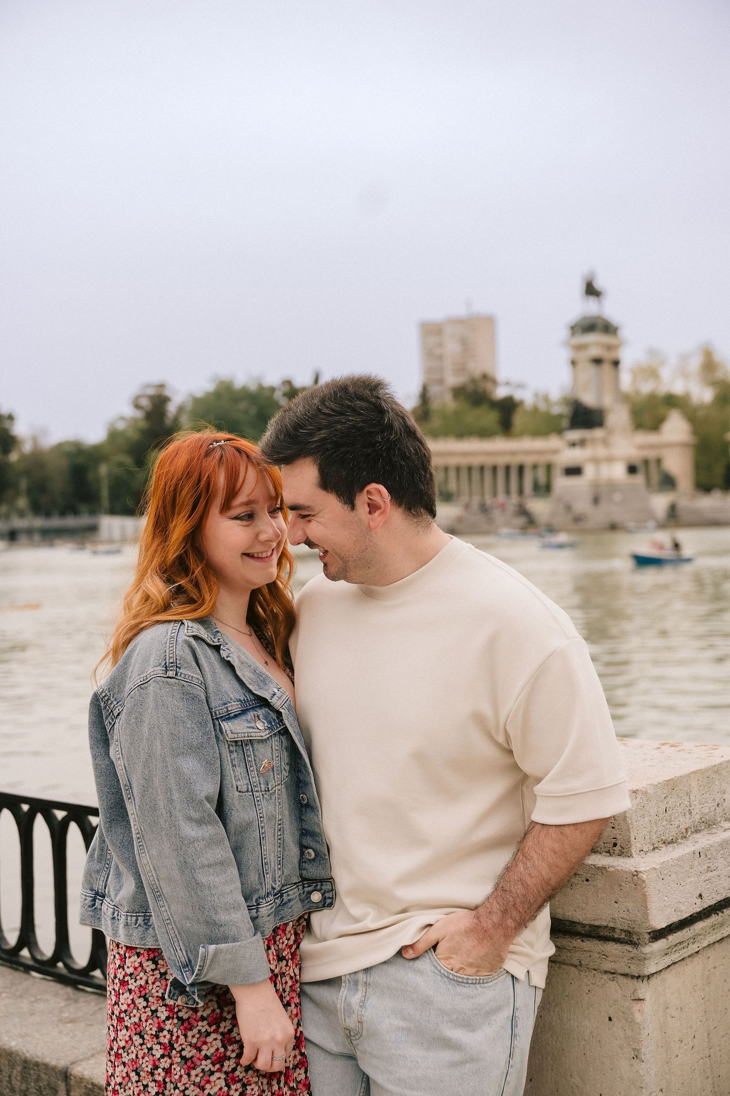A tender moment shared between a couple by a lake with monuments in the background.