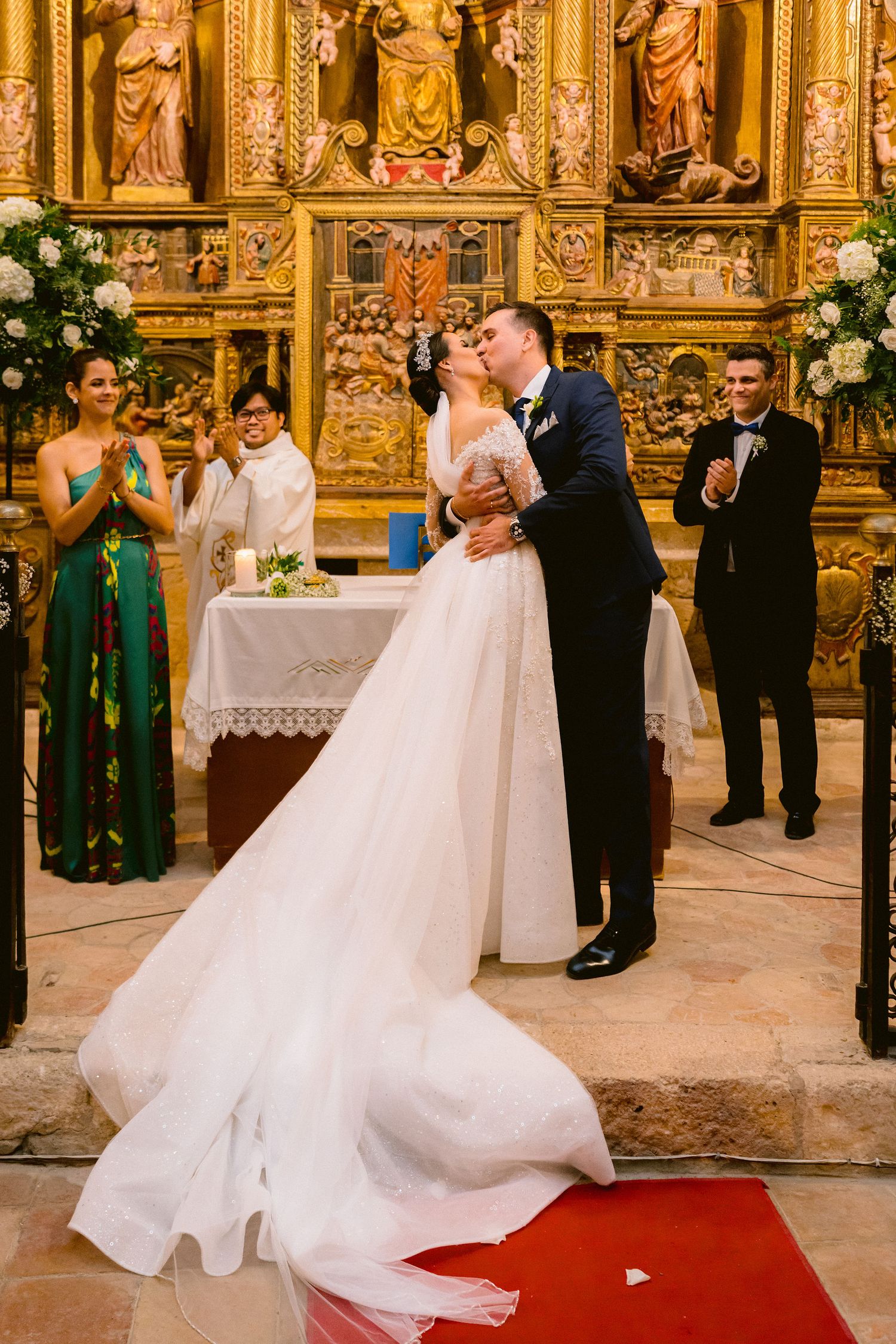 Wedding couple dances together during their first dance in an ornate cathedral with gold decor and a red carpet aisle.