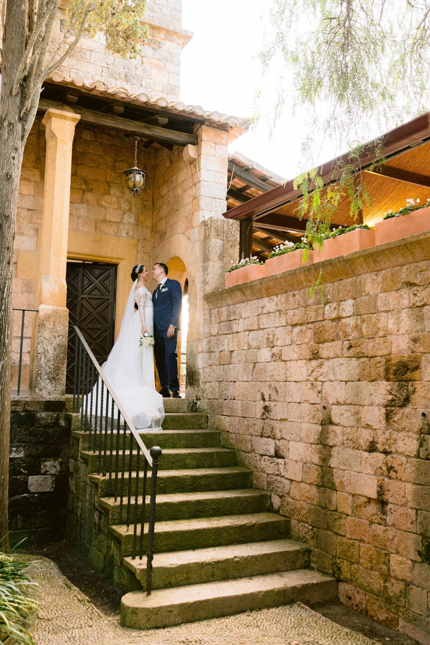 Couple ascending stone steps at a rustic Mediterranean villa with terracotta roof tiles and limestone walls.