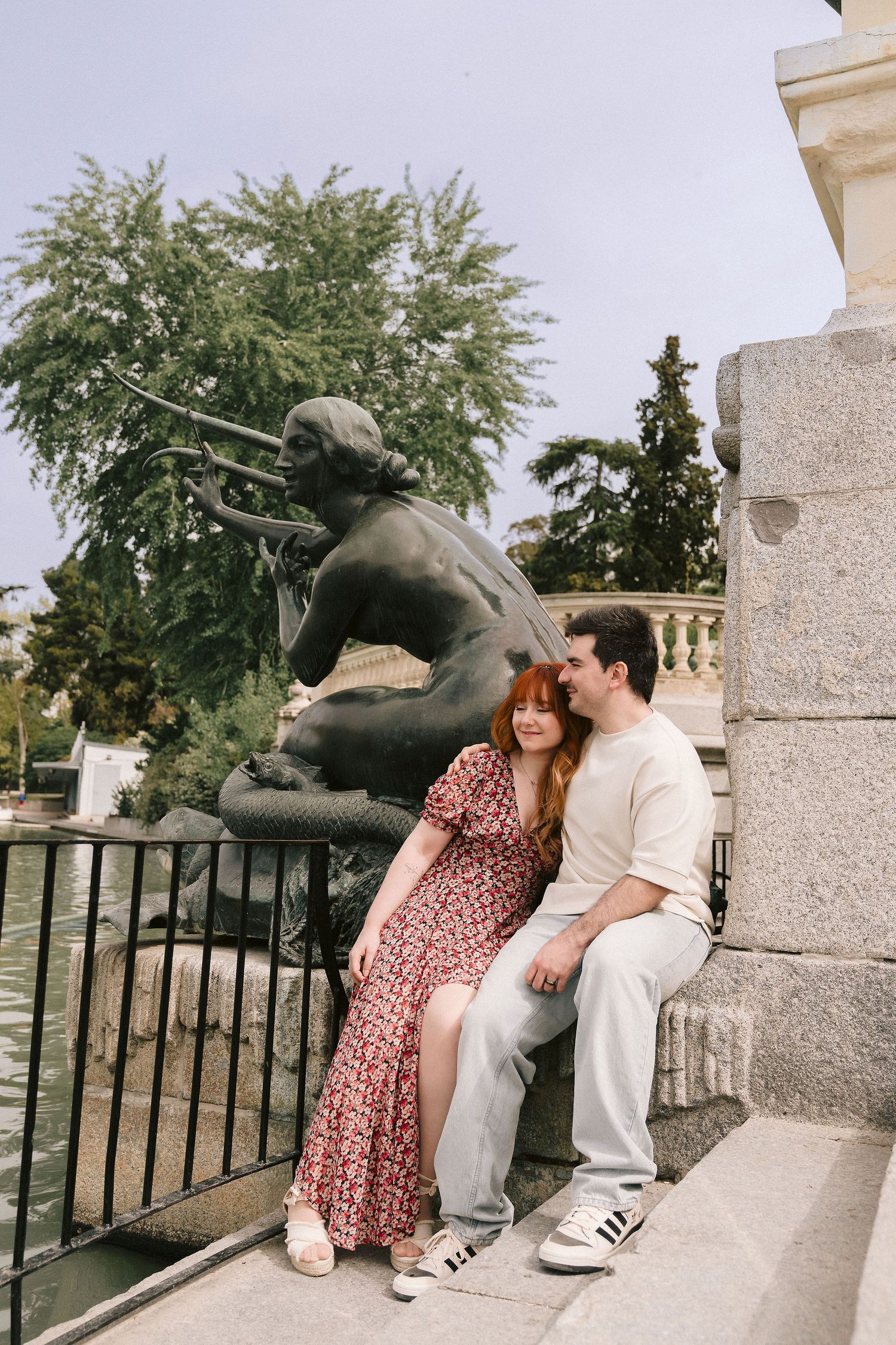 A couple rests near a bronze statue in a historic park setting.