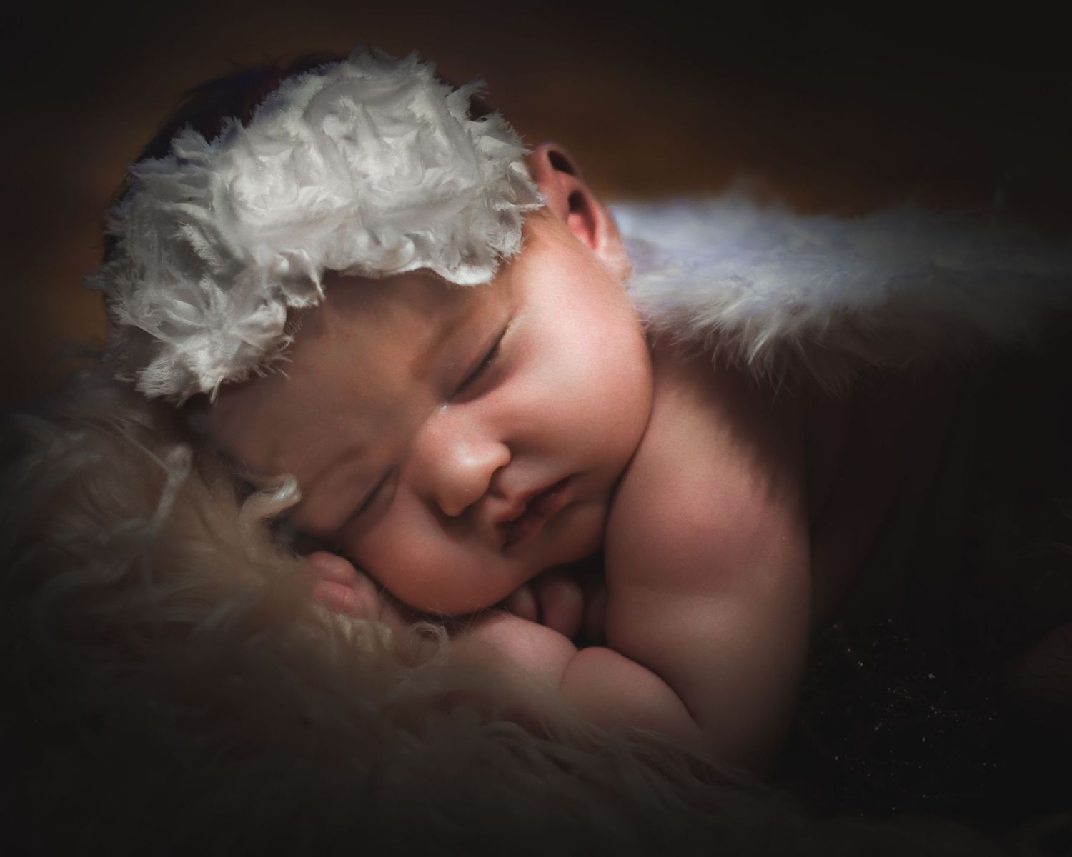 A series of soft-focus artistic photos showing a sleeping baby in dreamy lighting against a dark background.