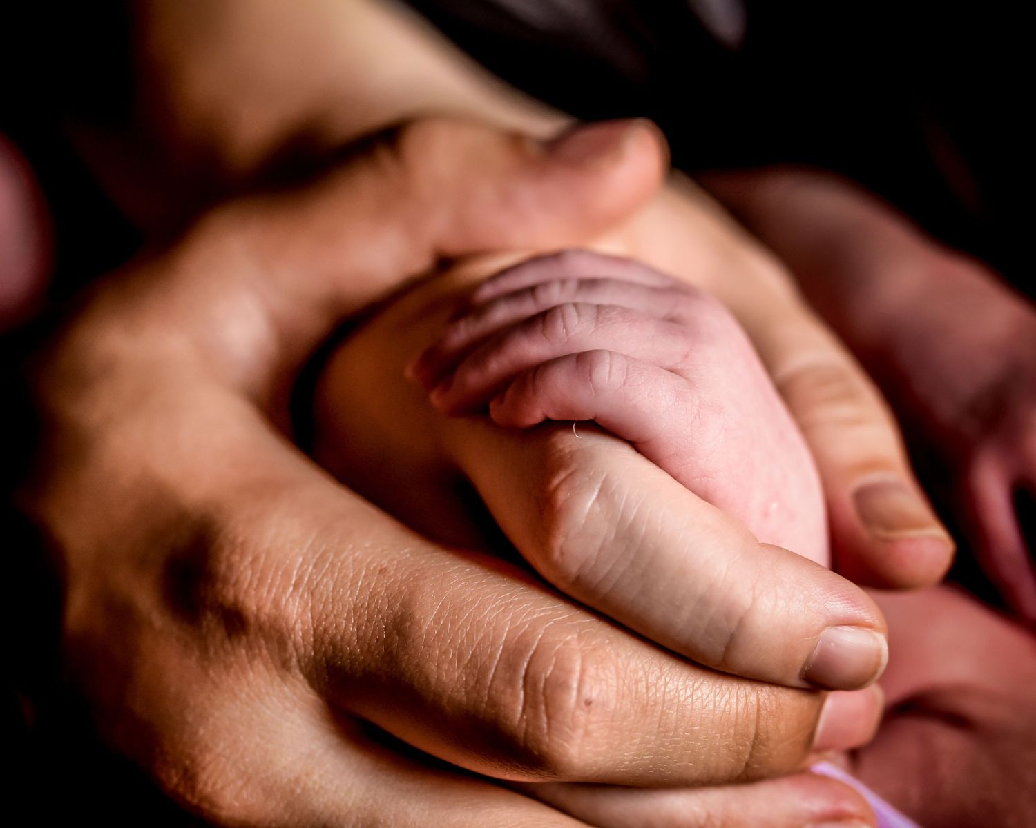 Close up of two hands tenderly touching and caressing each other against a dark background.