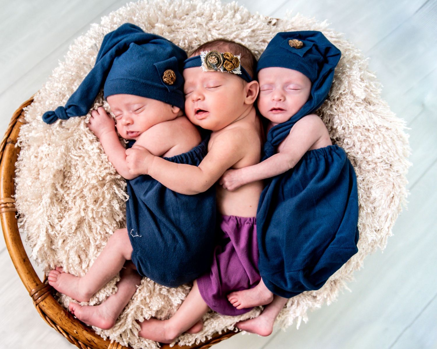 A sleeping newborn baby wrapped in navy blue swaddle lying in a woven basket on fluffy cream colored fur blanket.