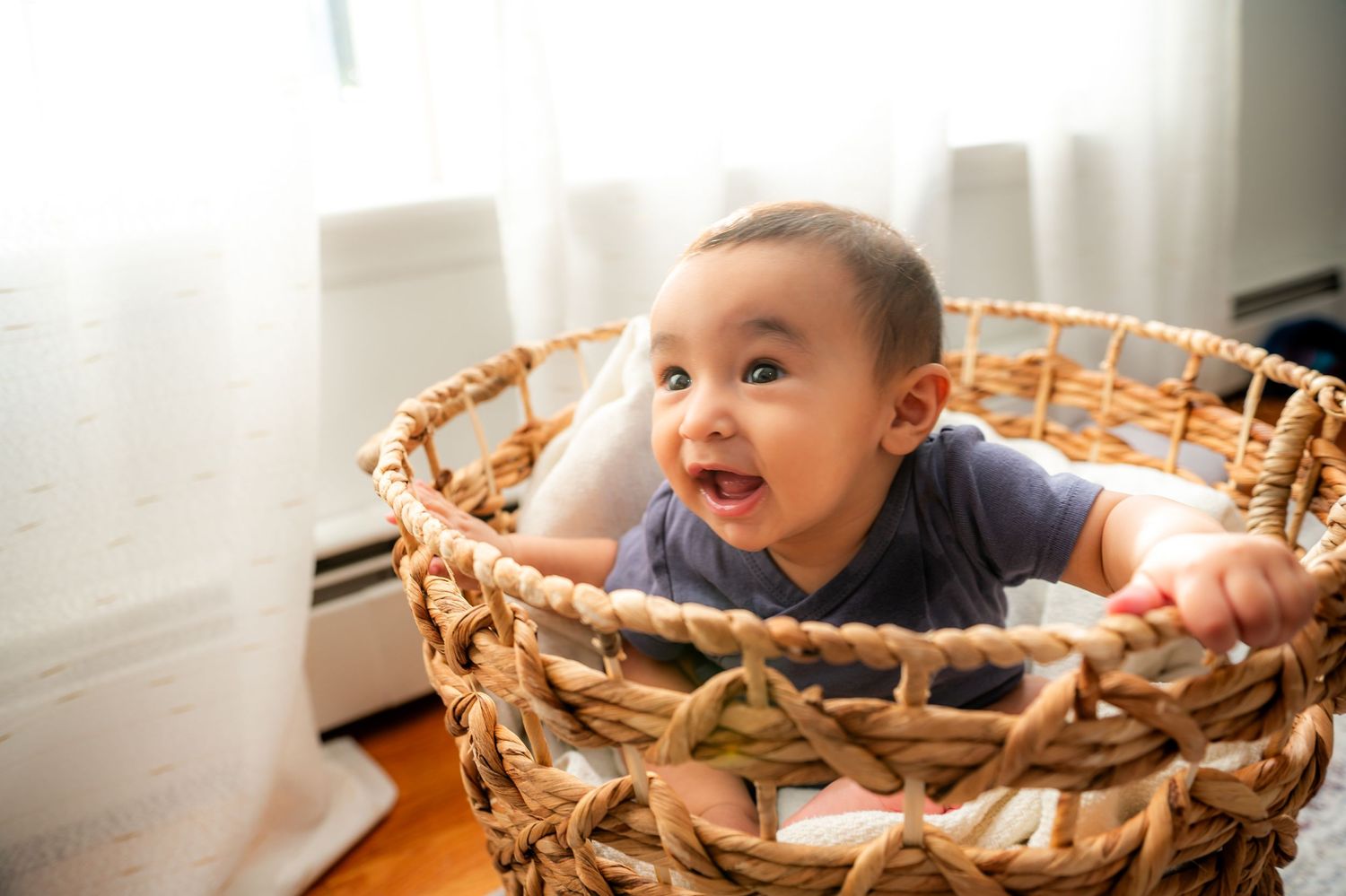 Baby lying in a woven basket smiles and plays while being photographed in a series of candid moments.