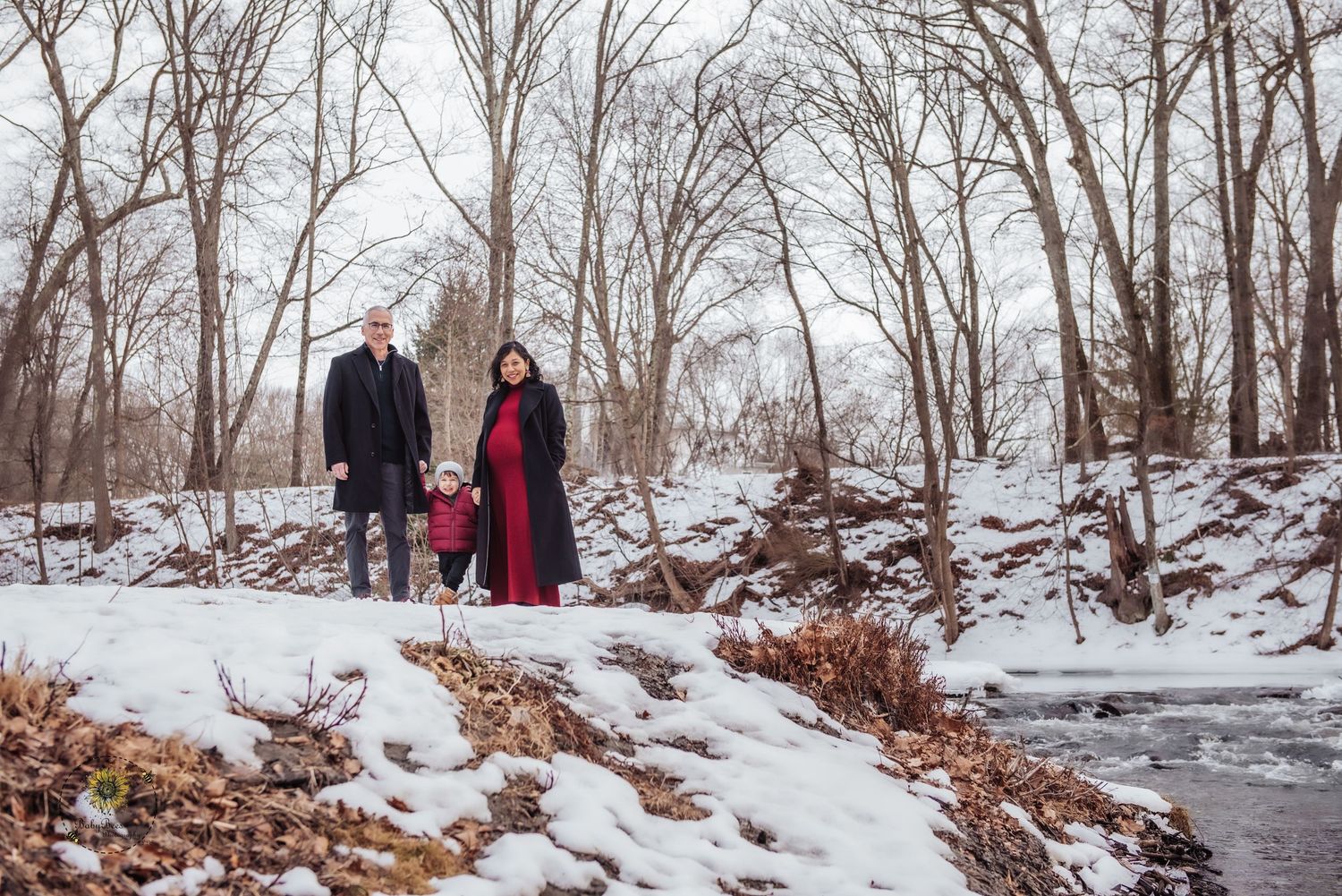 A couple walks together on a snowy winter path through bare trees in a serene forest landscape.