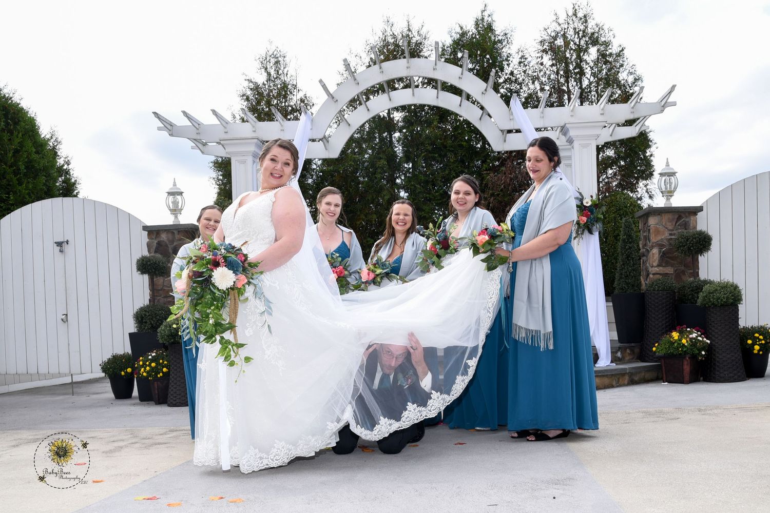 Wedding party members celebrate with playful poses under white garden arch.