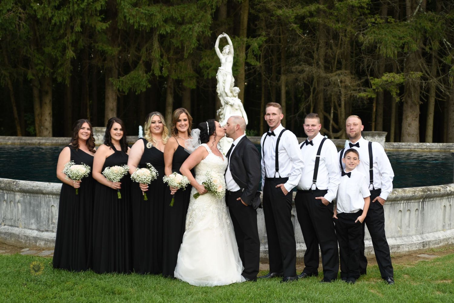 Wedding party in black and white attire posing outdoors for group photo.