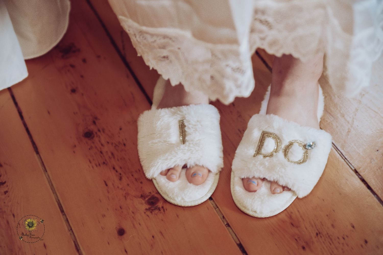 Cozy white wedding slippers with 'I DO' text on wooden flooring.