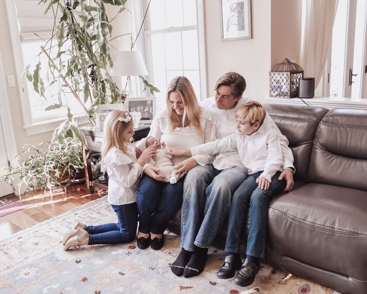 Family members sit together on a grey couch in a bright living room with white walls and indoor plants.