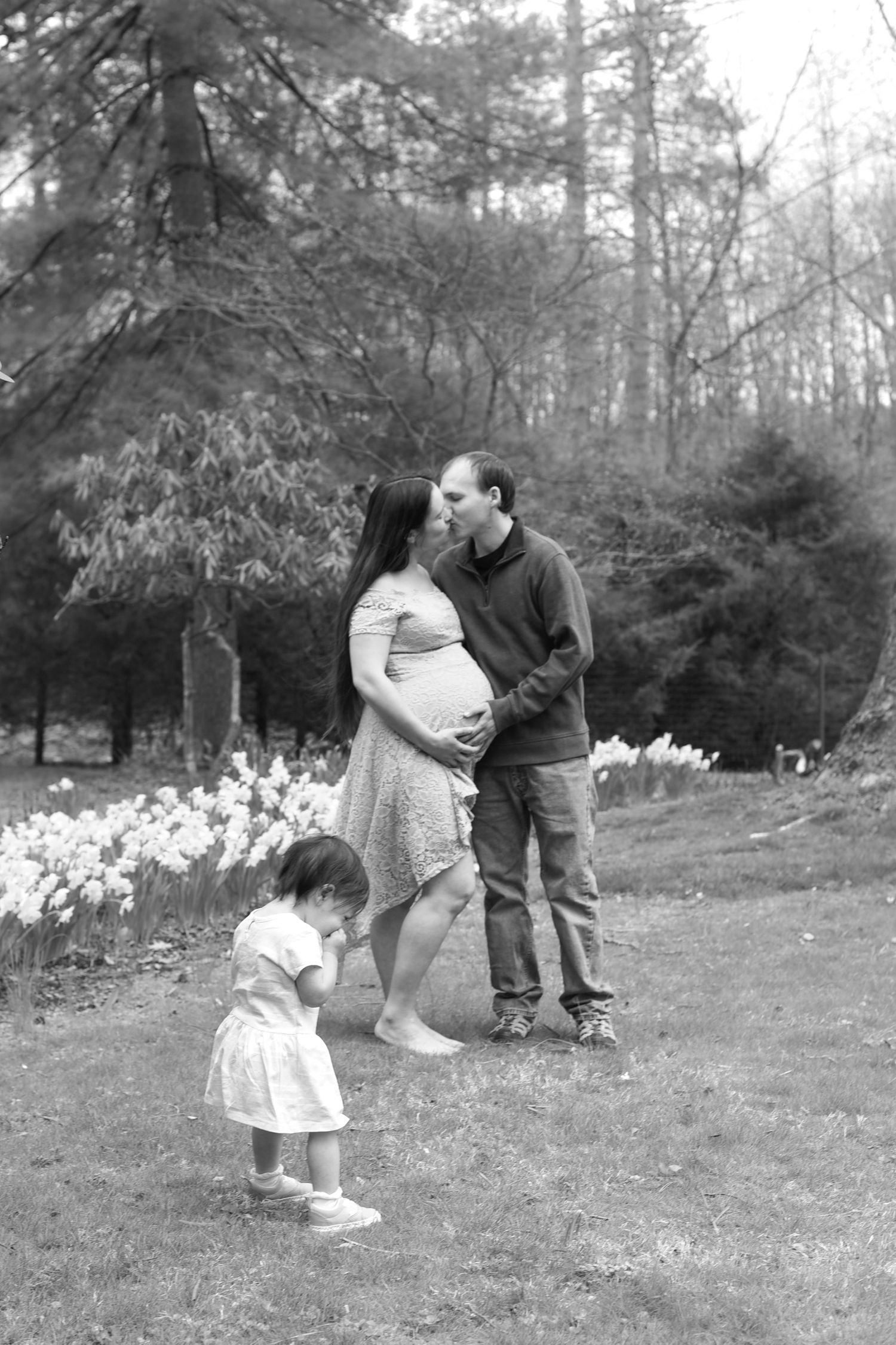 A tender black and white family moment outdoors with a small child in the foreground and daffodils blooming in spring.