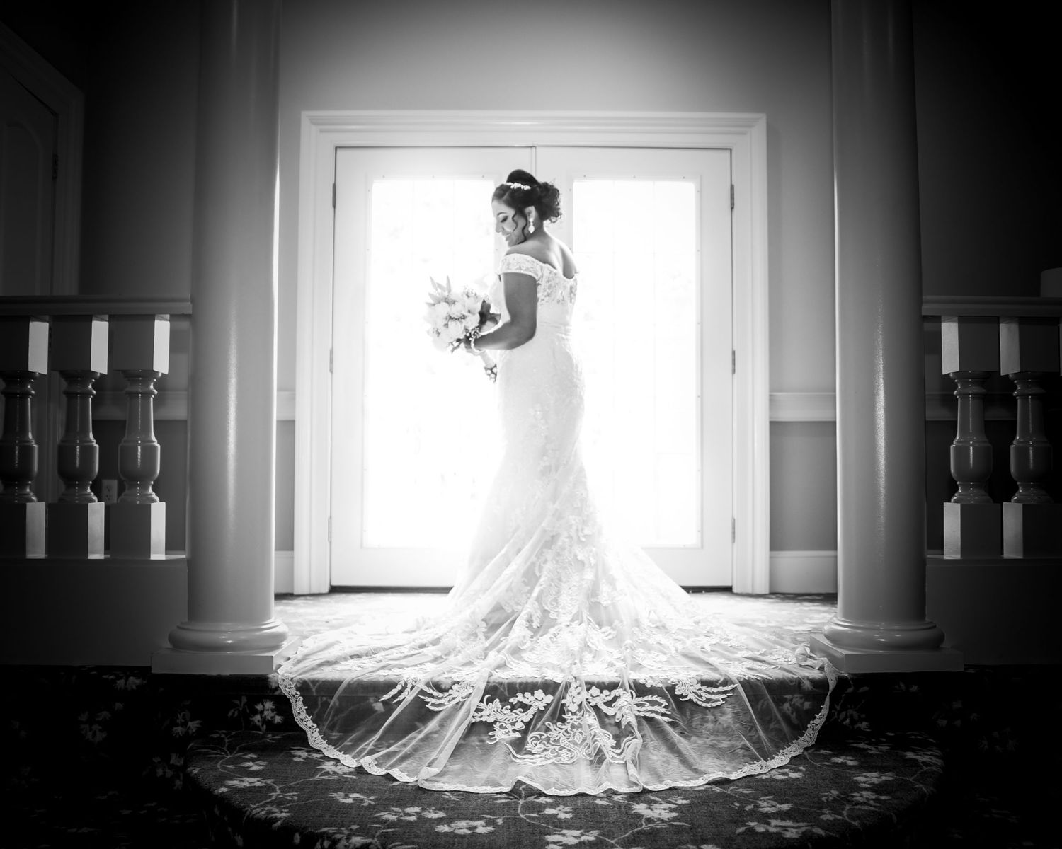 Dramatic black and white silhouette of bride in lace gown with long train standing in doorway.